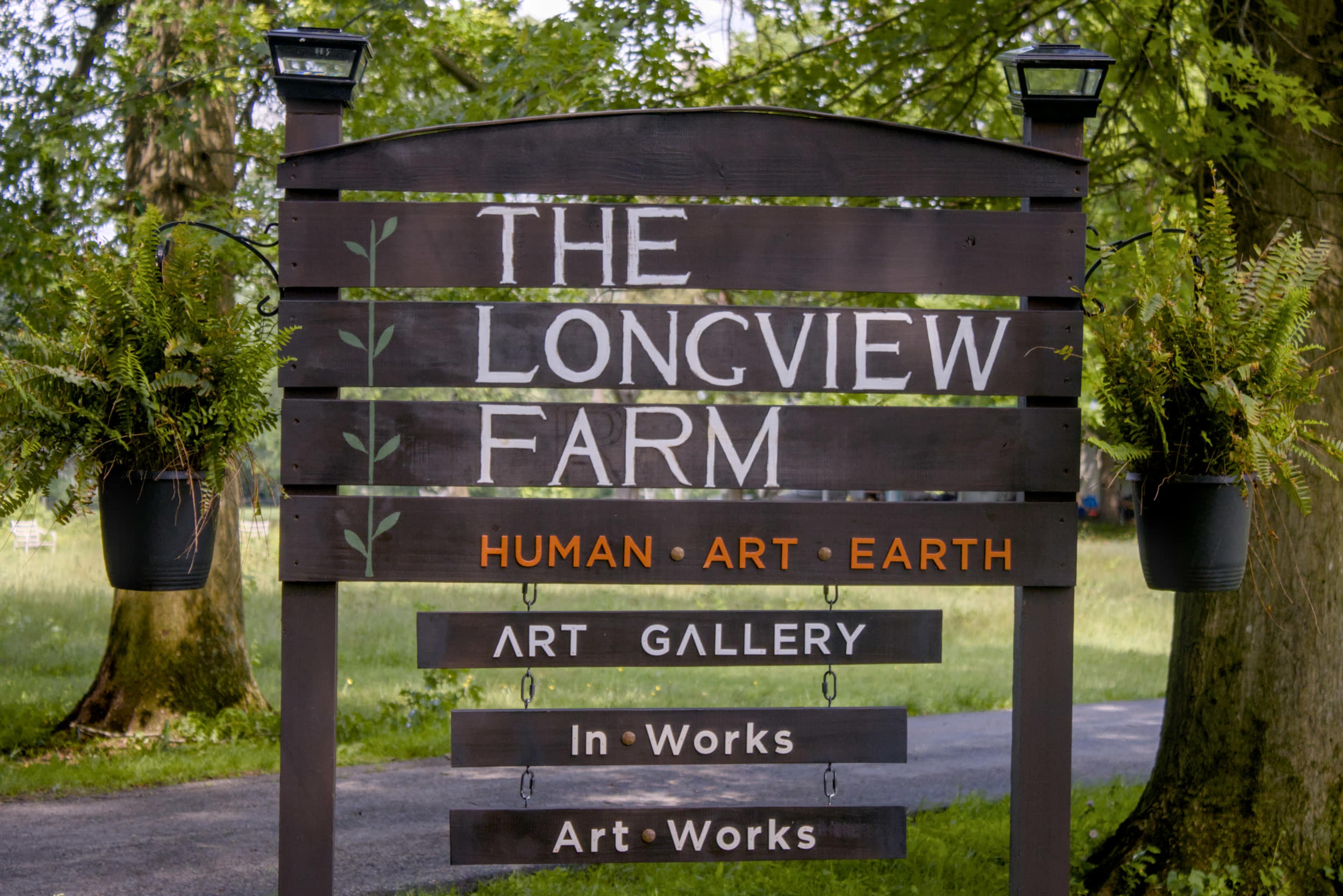 A wooden sign for "The Longview Farm" displays information about its focus on human, art, and earth, along with details about an art gallery.