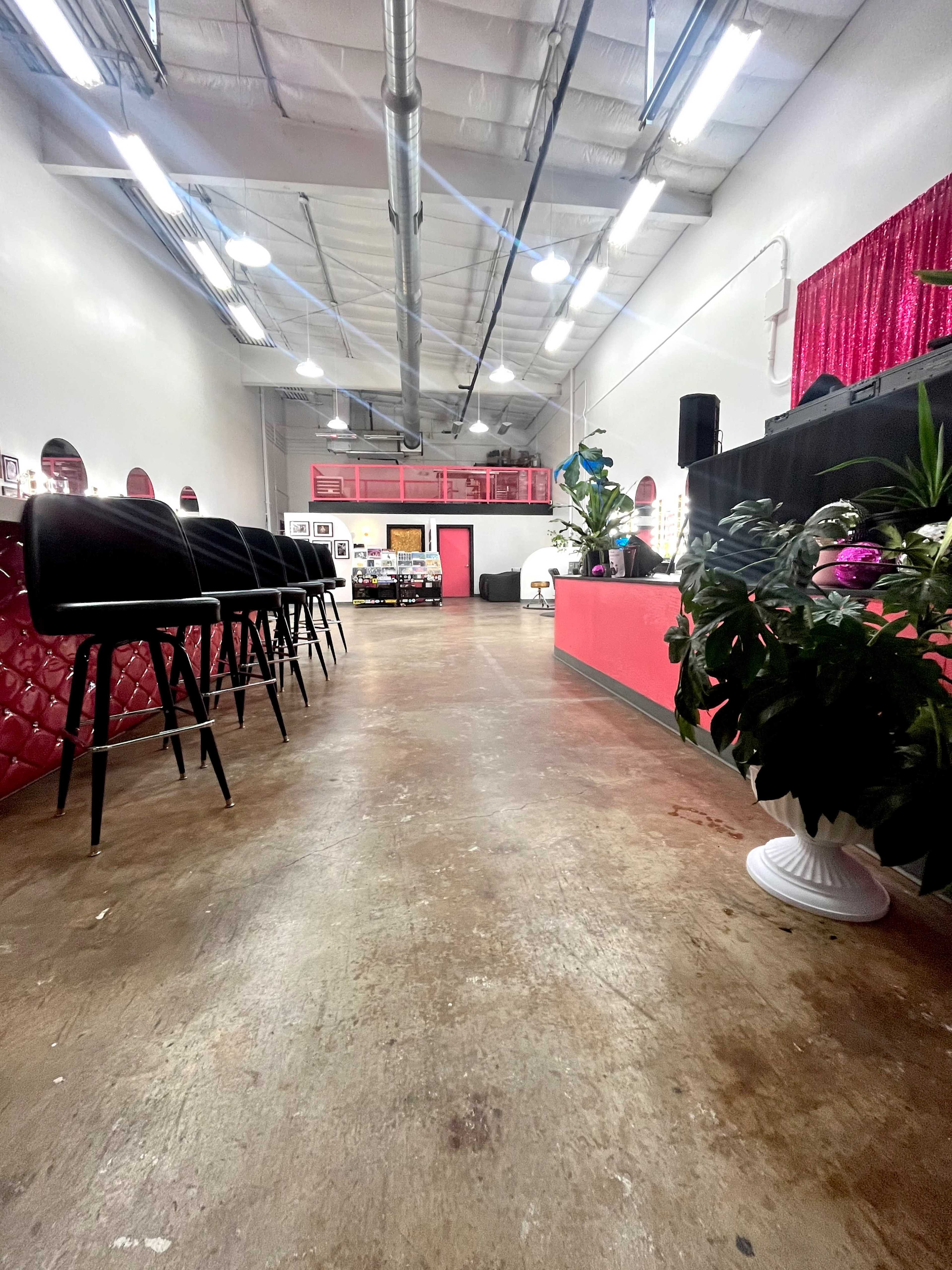 The image shows the interior of a modern salon with a polished floor, seating at a bar-style counter, and decorative plants in the foreground.