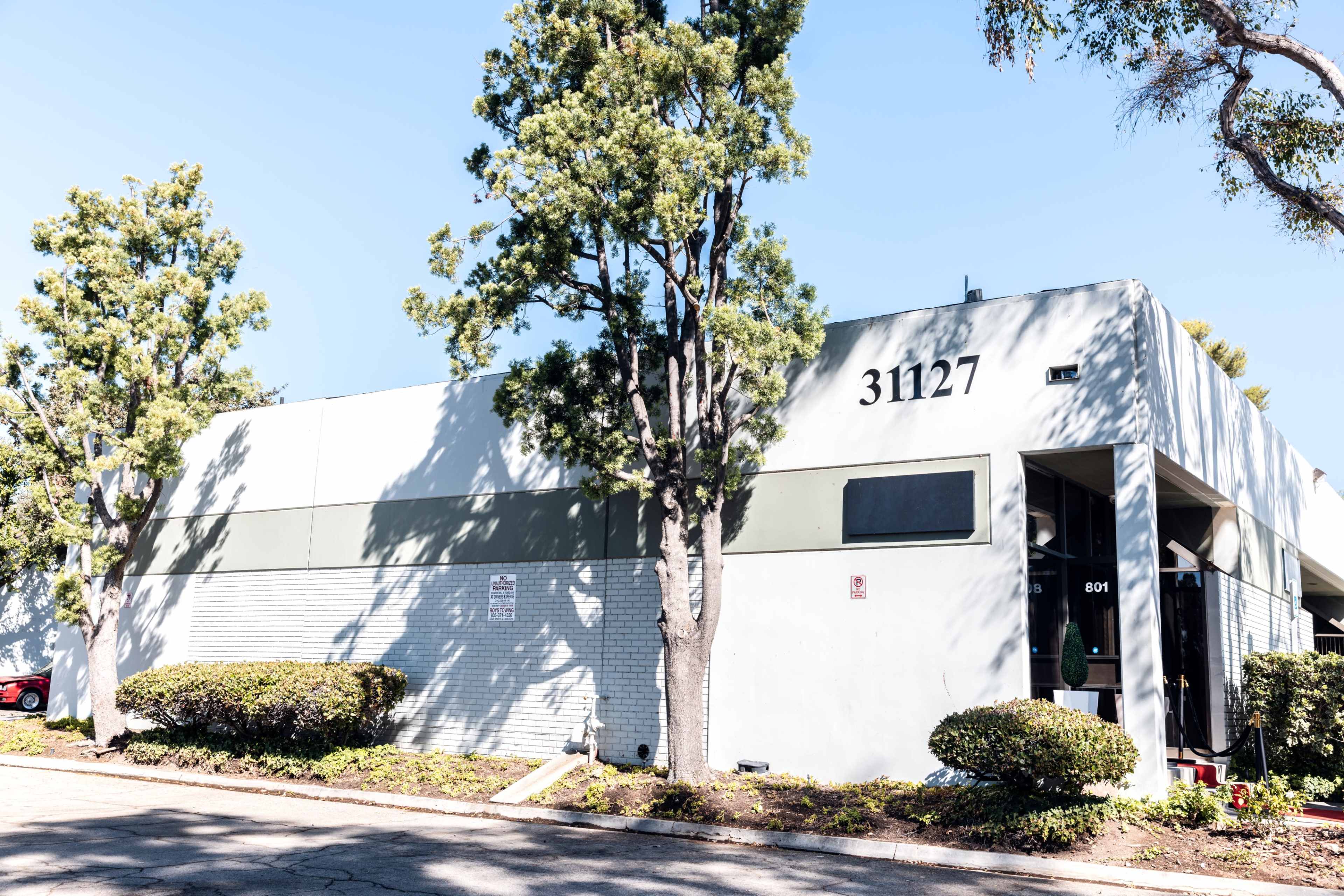 The image shows a gray commercial building with the address 31127, surrounded by neatly trimmed shrubs and trees.