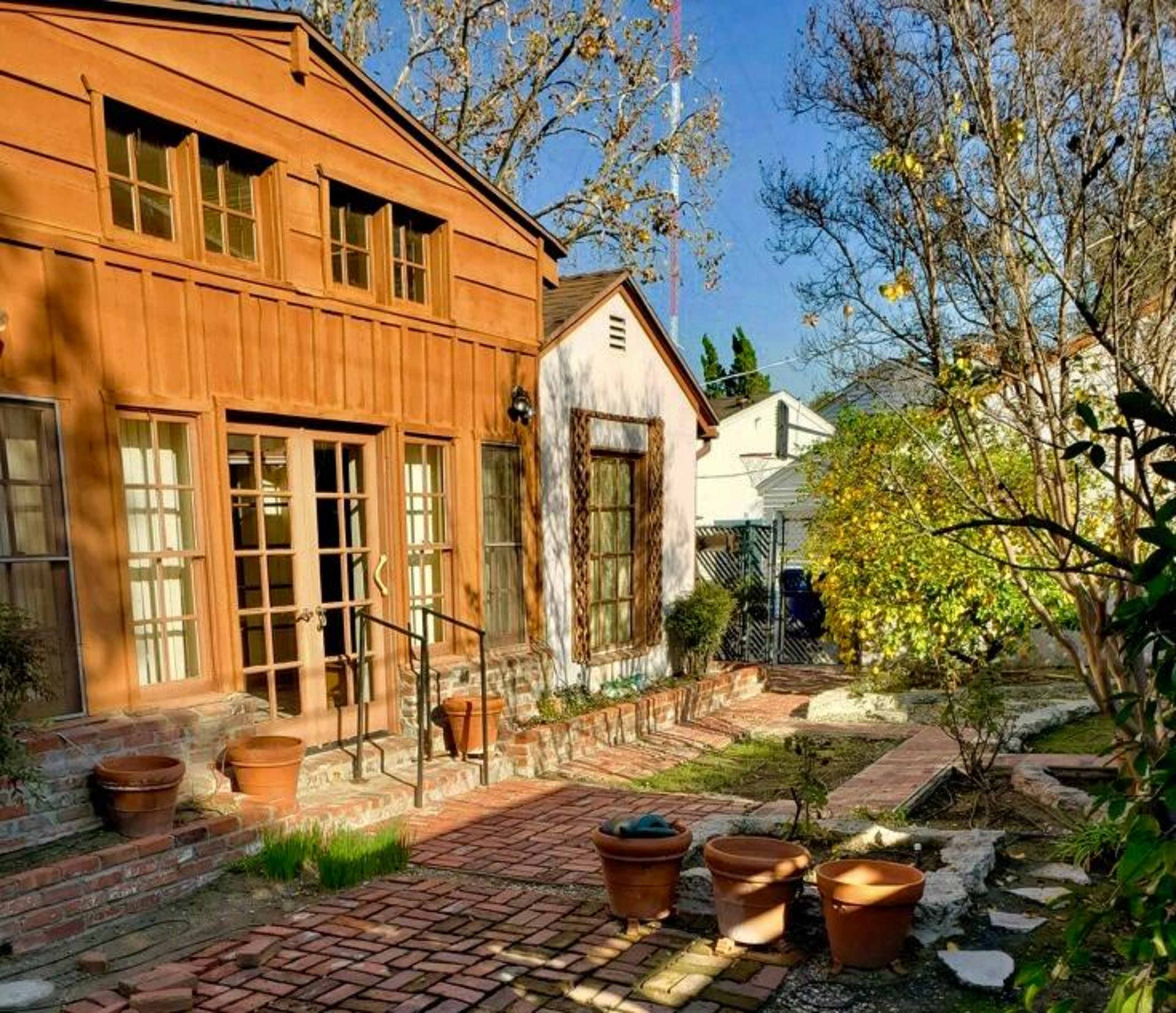 A charming house with a wooden facade and a brick pathway leading to a well-maintained garden with potted plants.