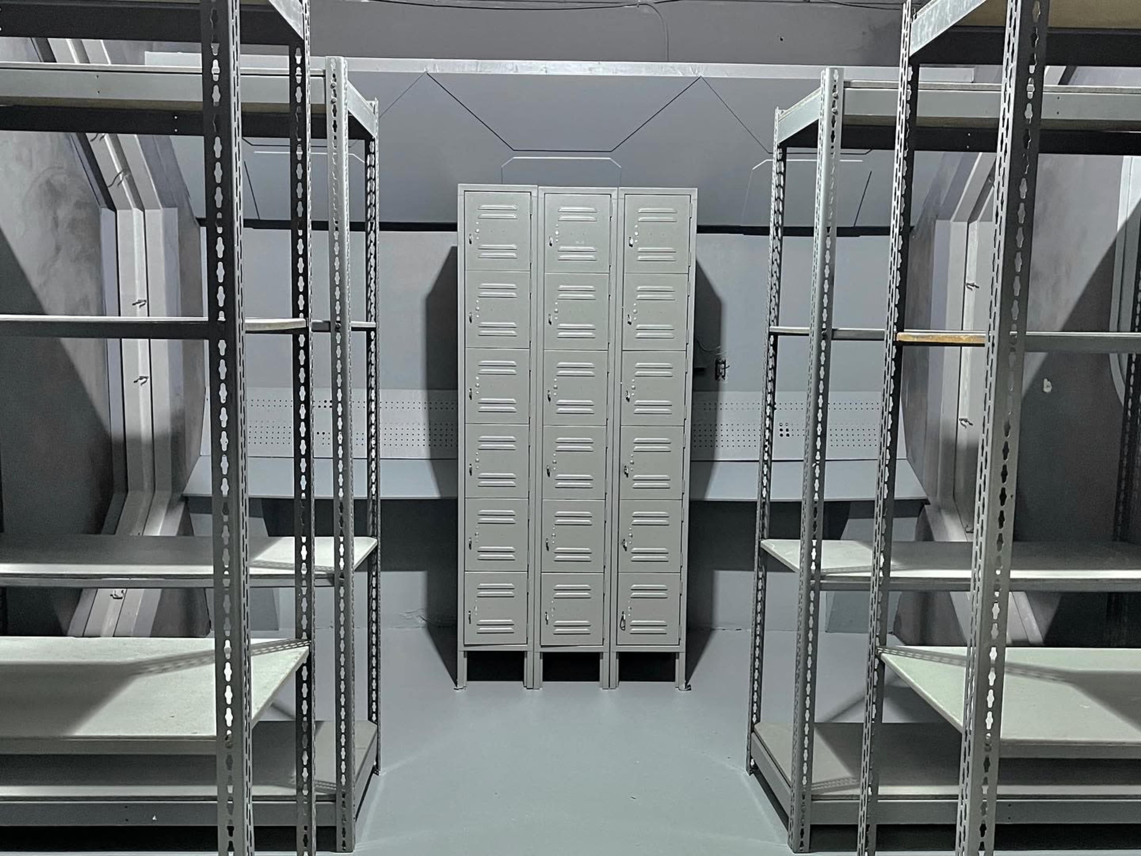 A minimalist room with metal shelves and a row of gray lockers in the center.
