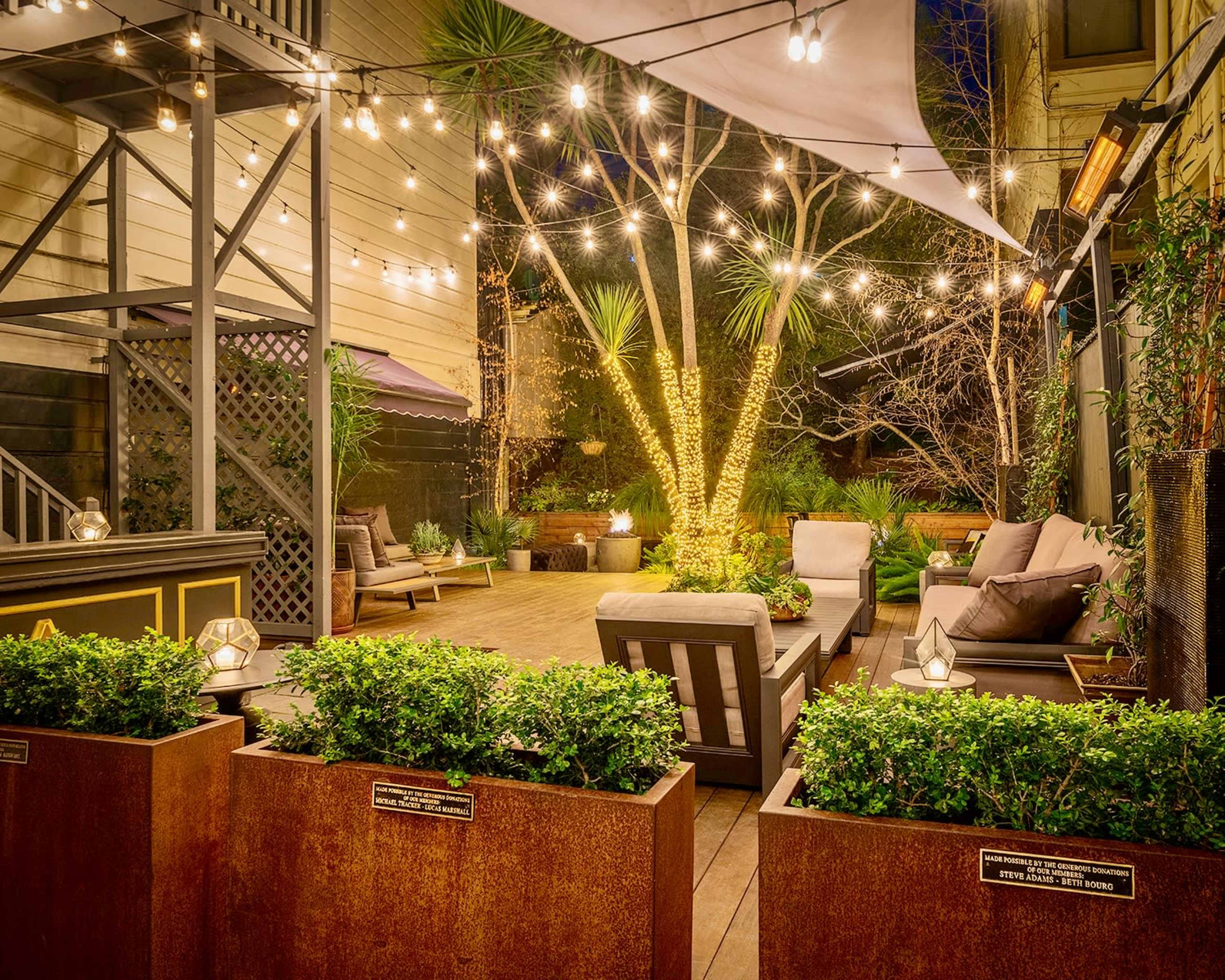 A landscaped outdoor patio area with string lights, seating arrangements, and potted plants.