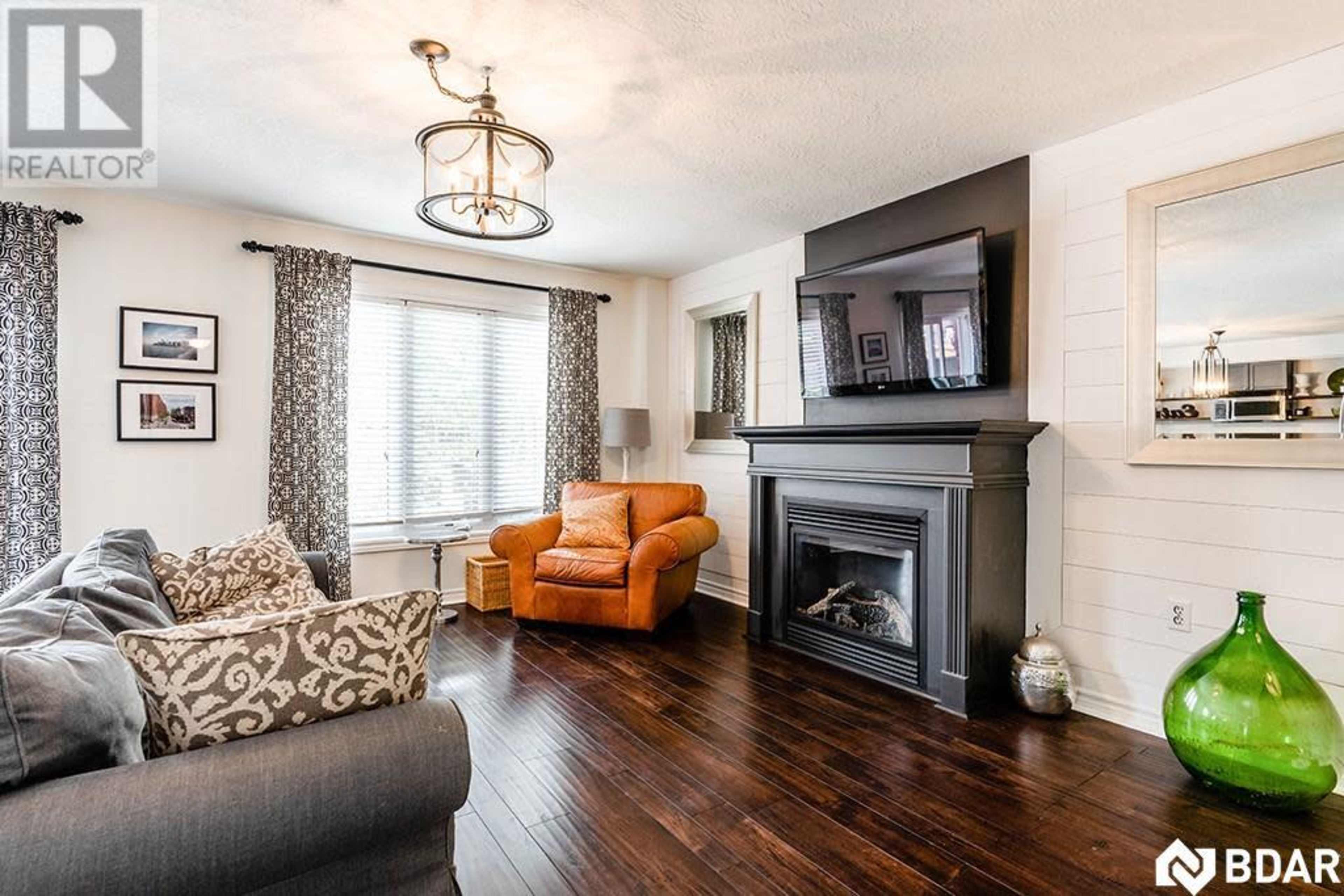 The living room features a brown leather armchair, a black fireplace, and a large wall-mounted television, with large windows allowing natural light.