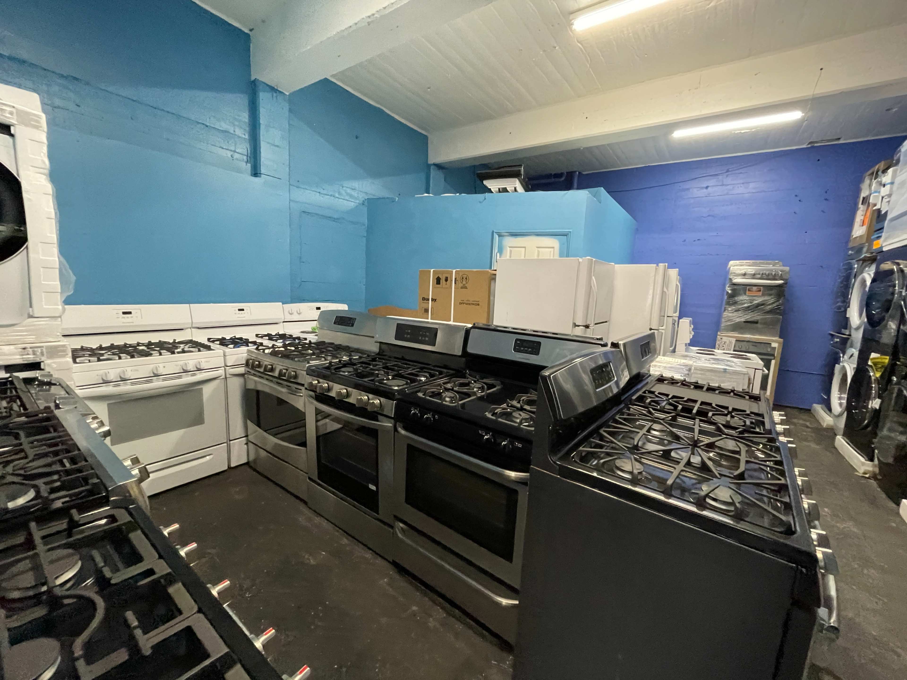The image shows a store interior with various kitchen appliances, including gas stoves and refrigerators, arranged against blue-painted walls.