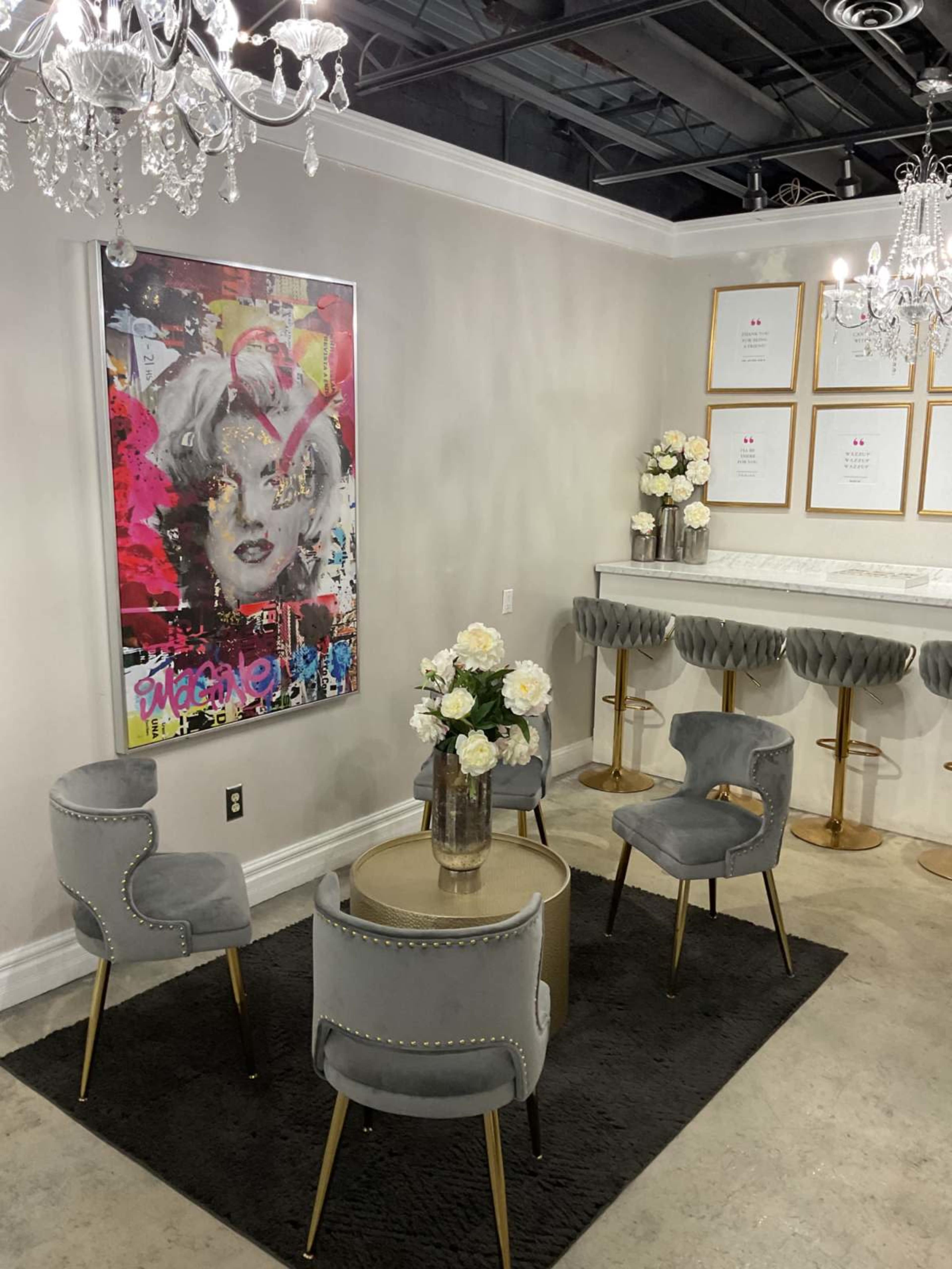 The image shows a stylish lounge area with gray upholstered chairs, a round table, a floral arrangement, and a colorful artwork on the wall.