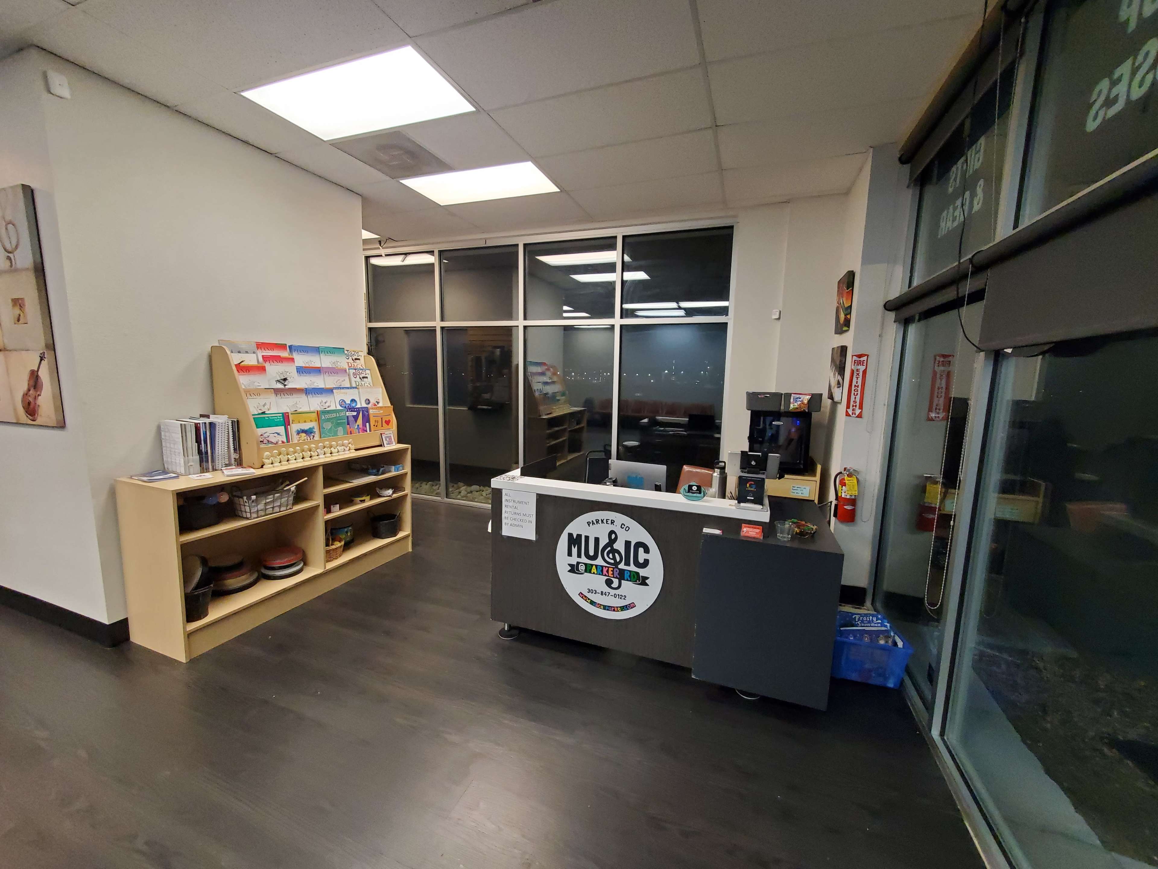 The image shows a music-oriented reception area with shelves displaying materials and a front desk featuring a logo.