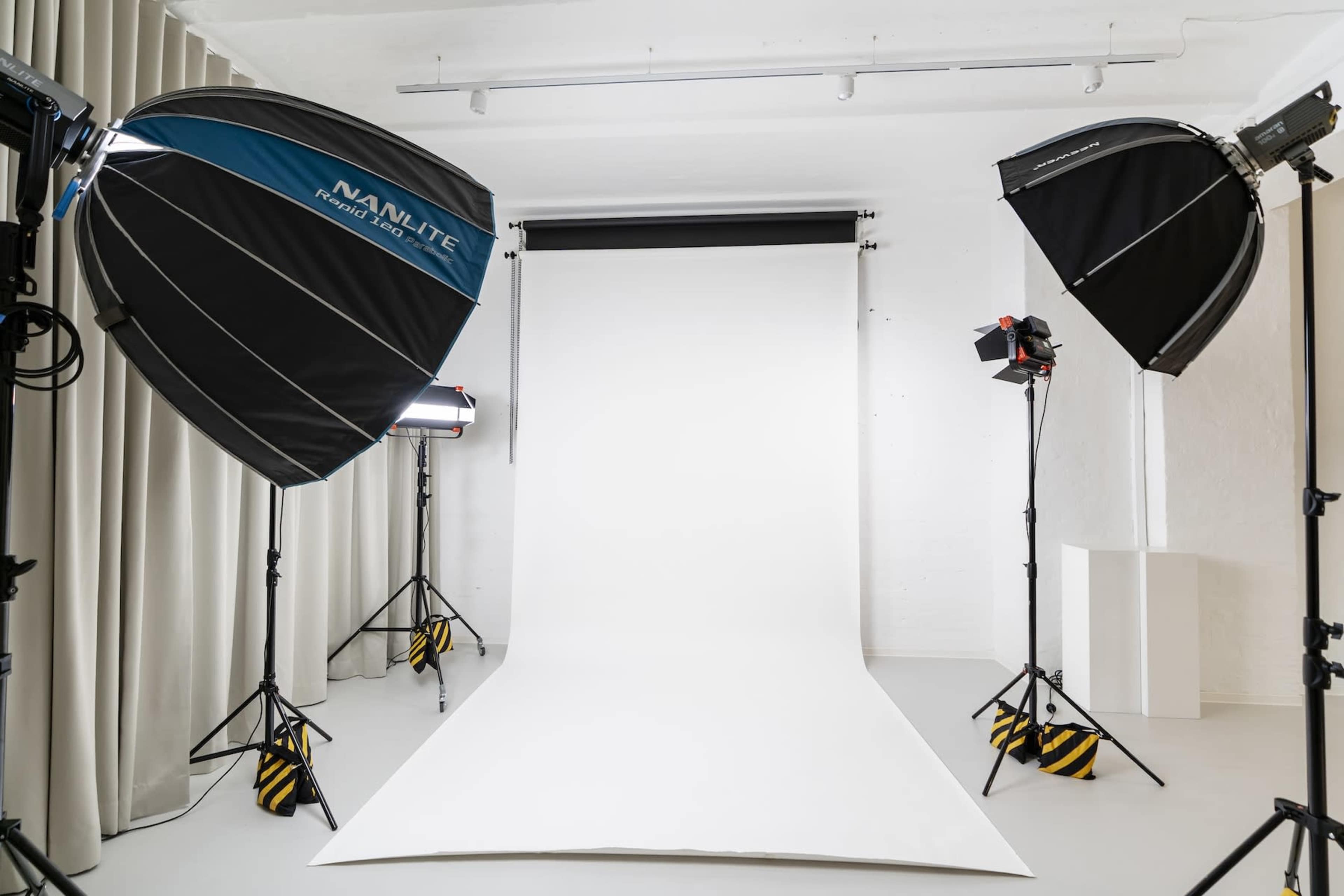 The image shows a photography studio with two large softbox light setups and a white backdrop on the floor.