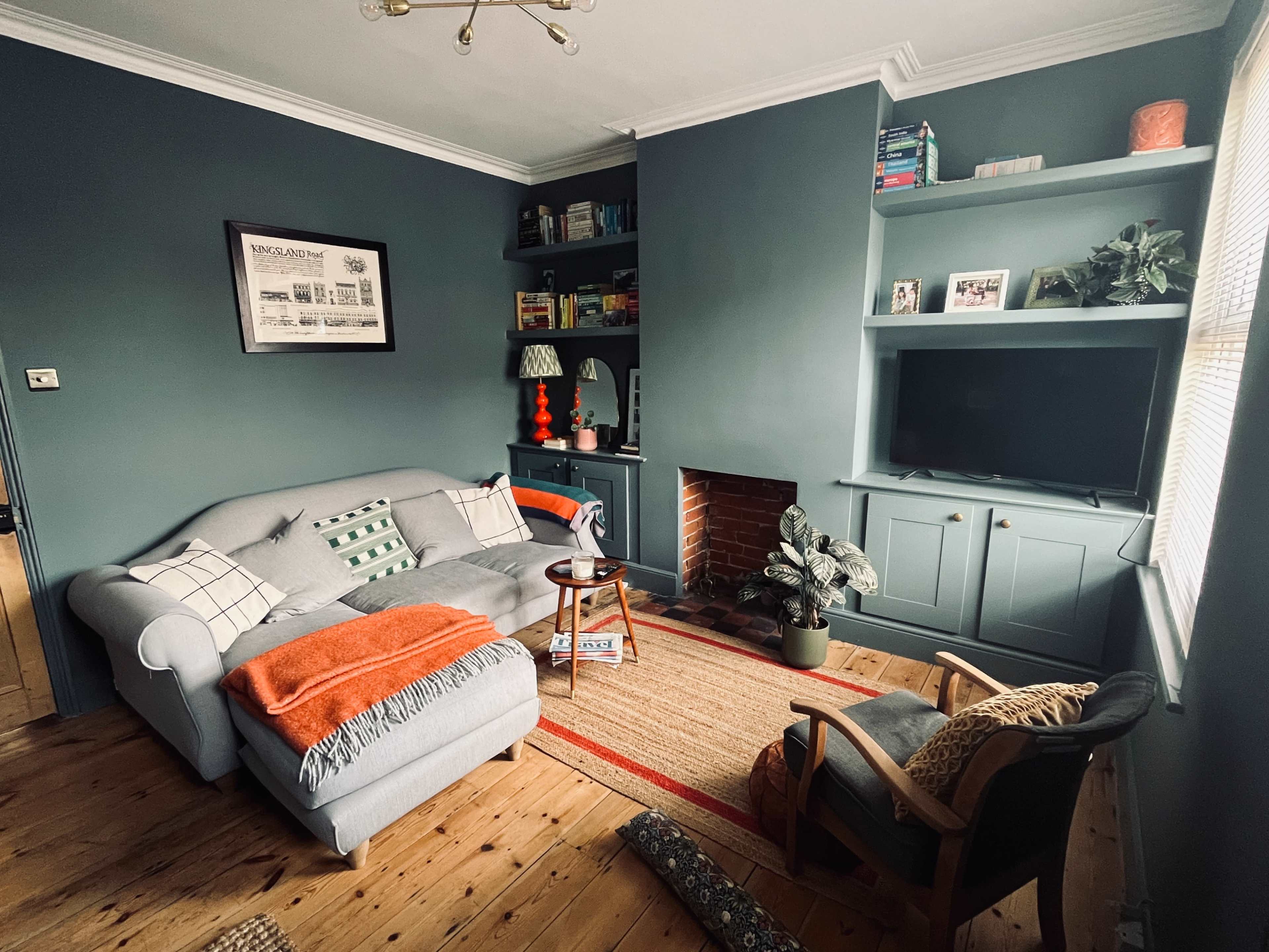 A cozy living room featuring a gray sofa, a small wooden table, and a fireplace, with shelves filled with books and decorative items.