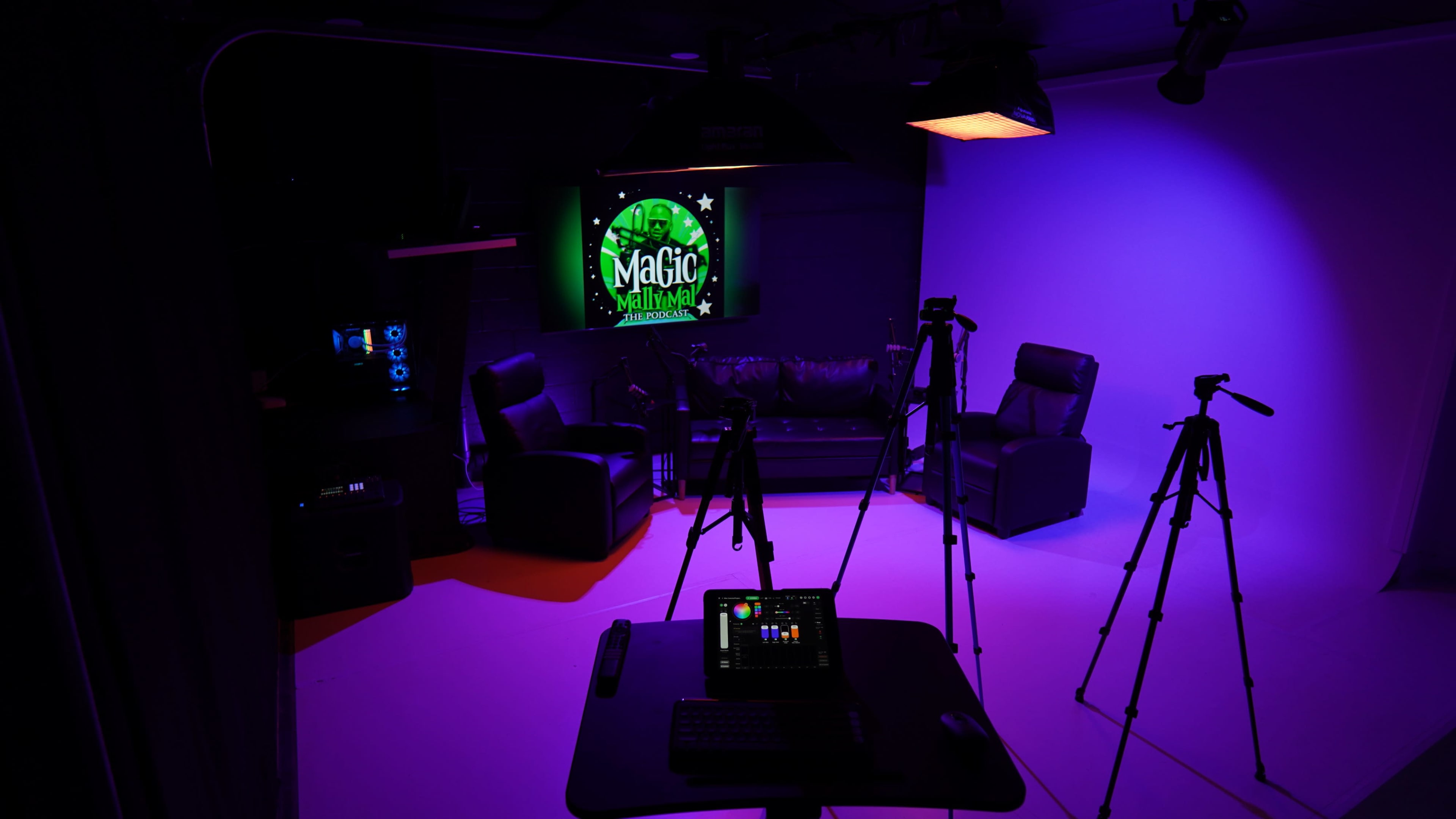 The image shows a soundstage setup with two black leather chairs, multiple tripods, and a colorful backdrop featuring a "Magic" sign.