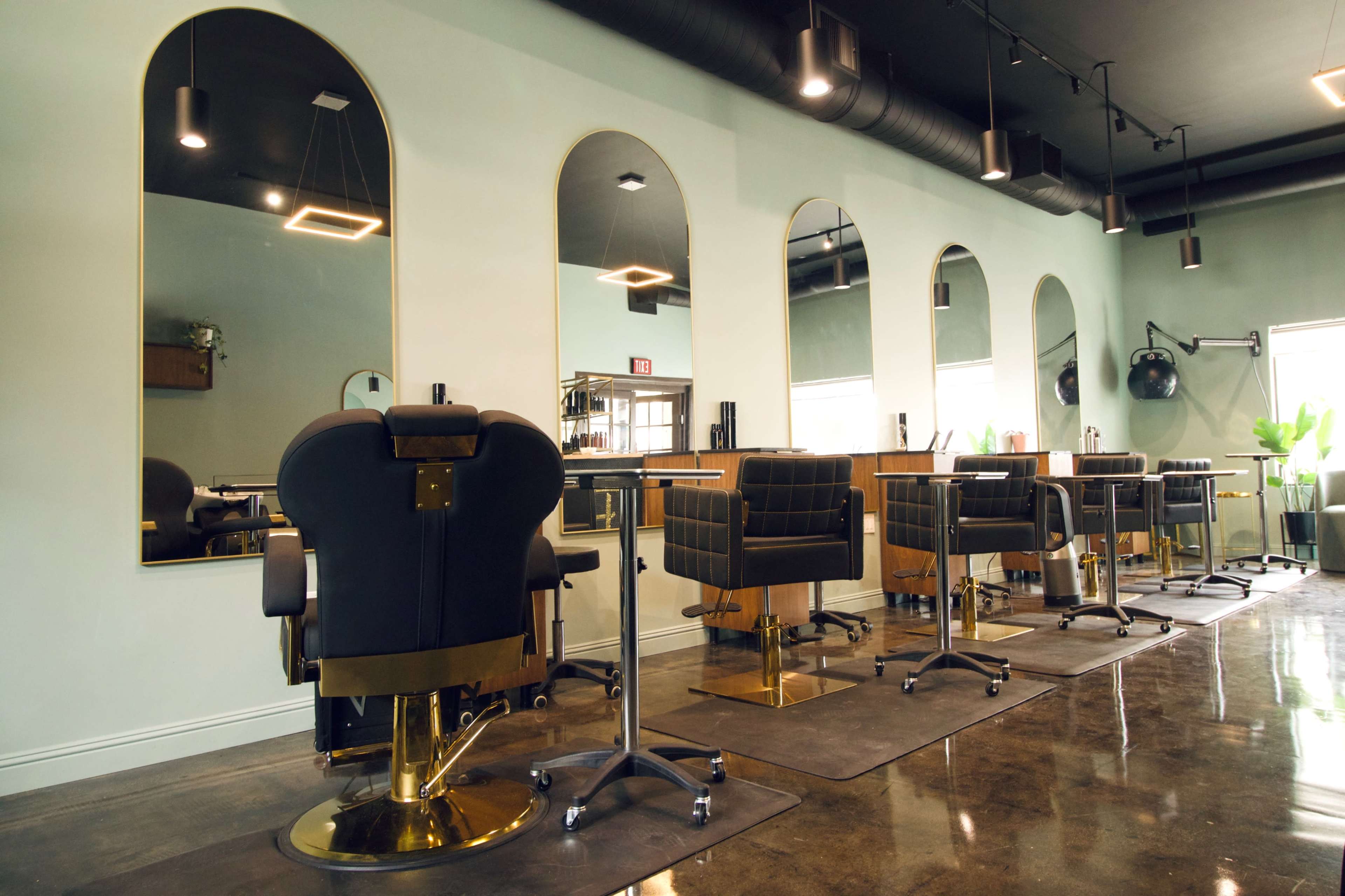 The image shows a modern hair salon with several black styling chairs arranged in front of wall-mounted mirrors.