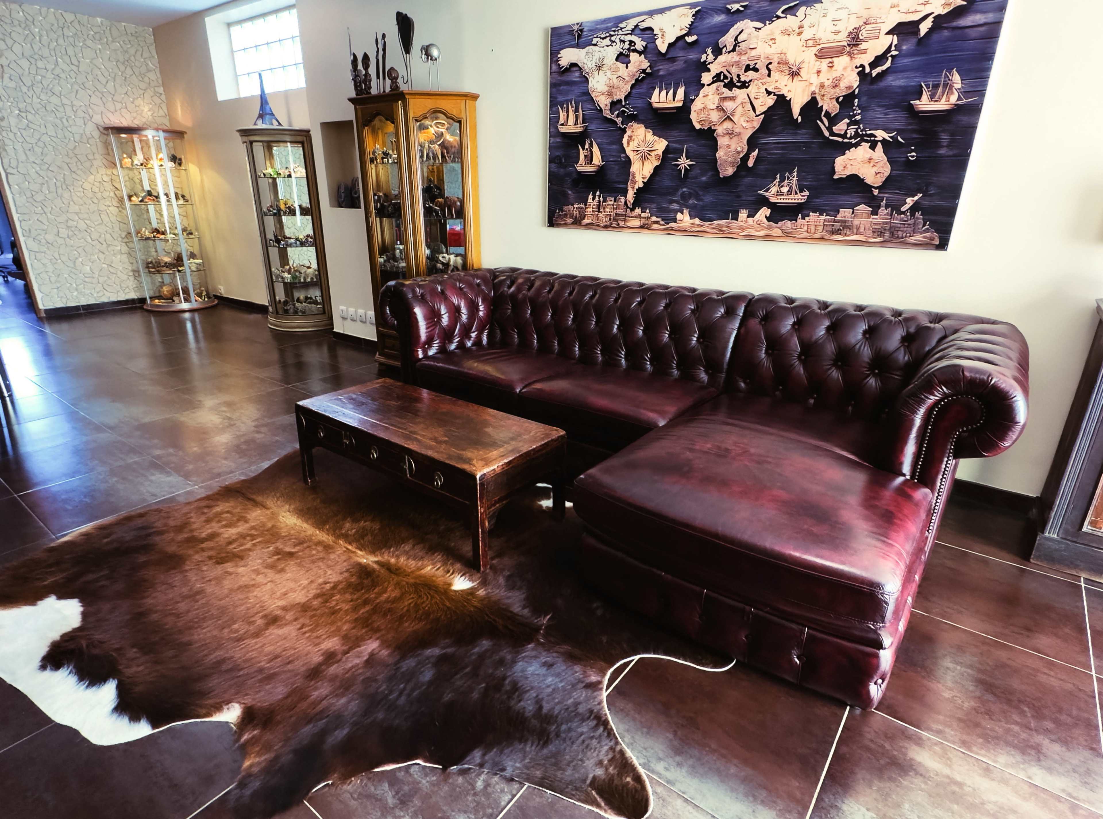 The image shows a stylish living room featuring a burgundy leather chesterfield sofa, a wooden coffee table, and a decorative world map mounted on the wall.