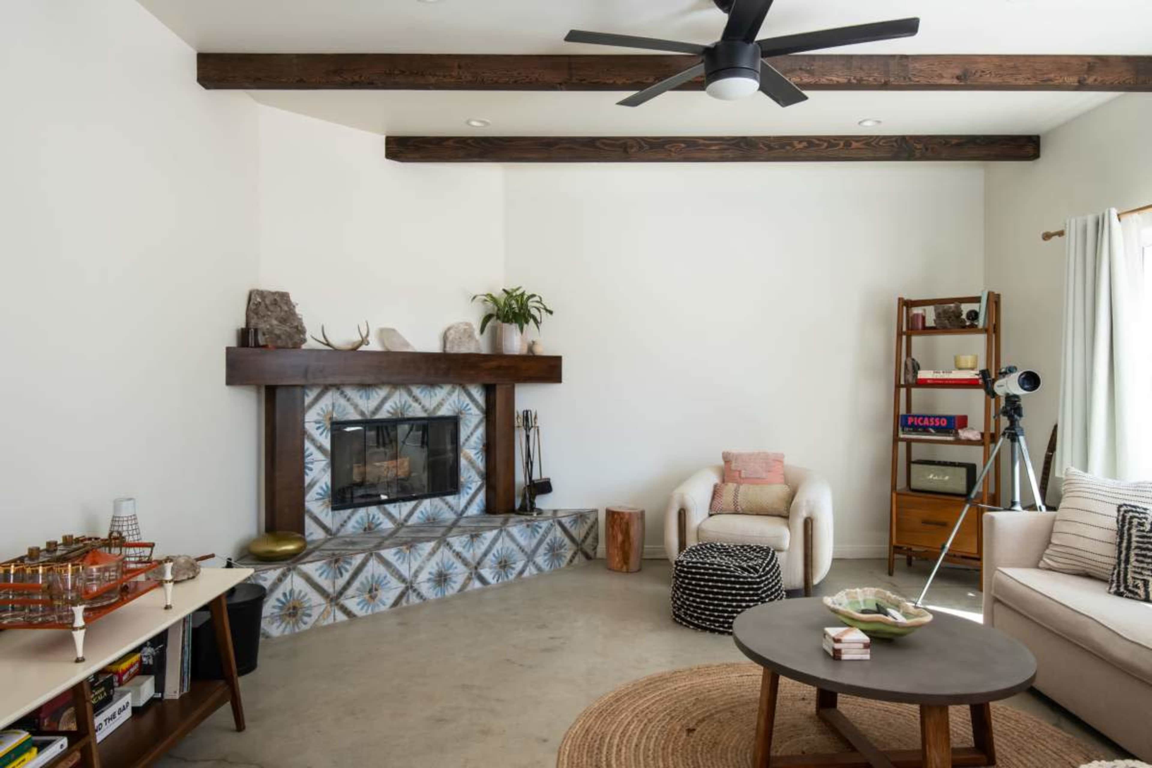 The image shows a modern living room featuring a fireplace with patterned tiles, a circular coffee table, a bookshelf with various items, and a comfortable seating arrangement.