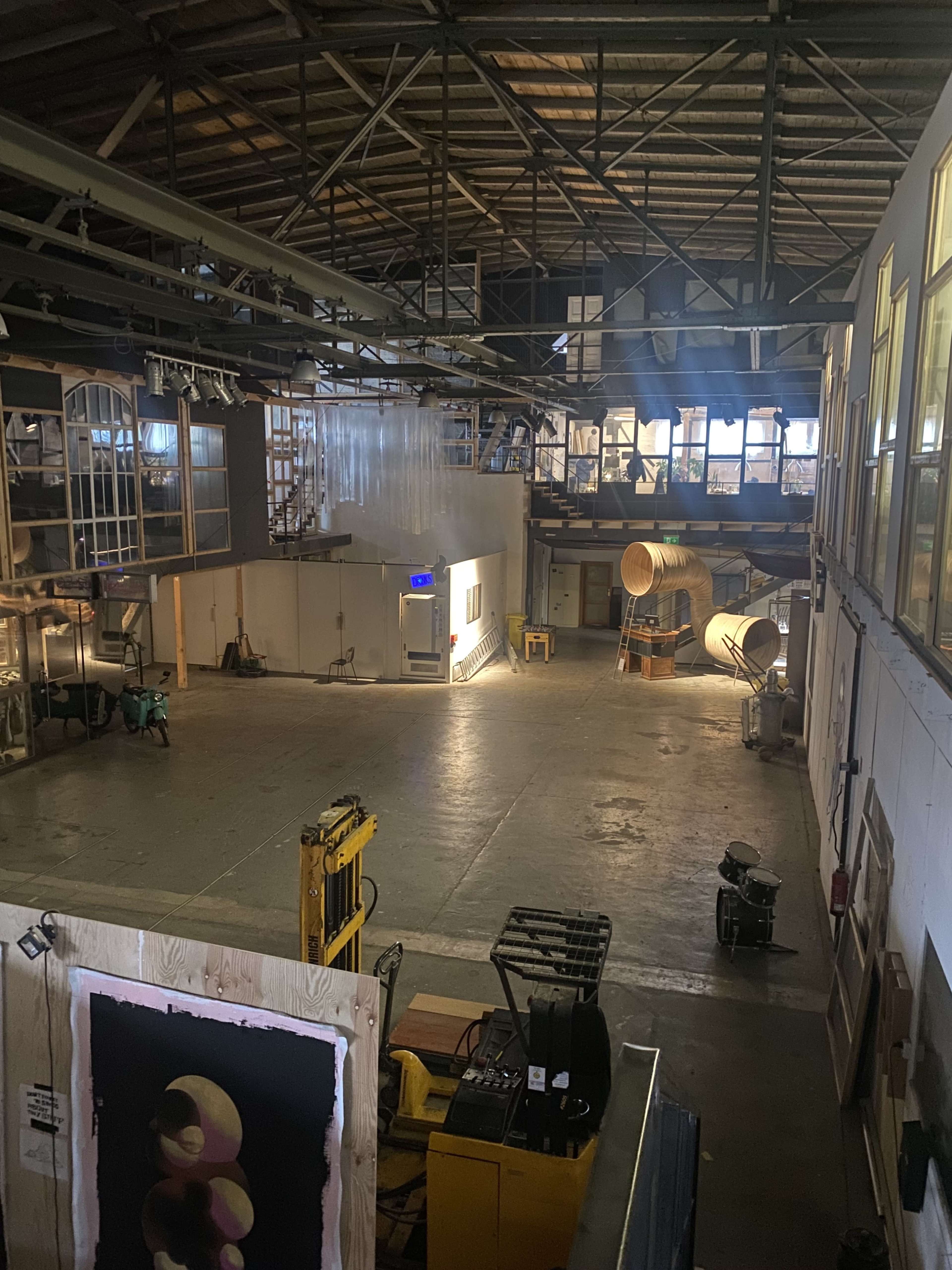 The image shows an industrial space with high ceilings, large windows, and various machinery in a brightly lit area.