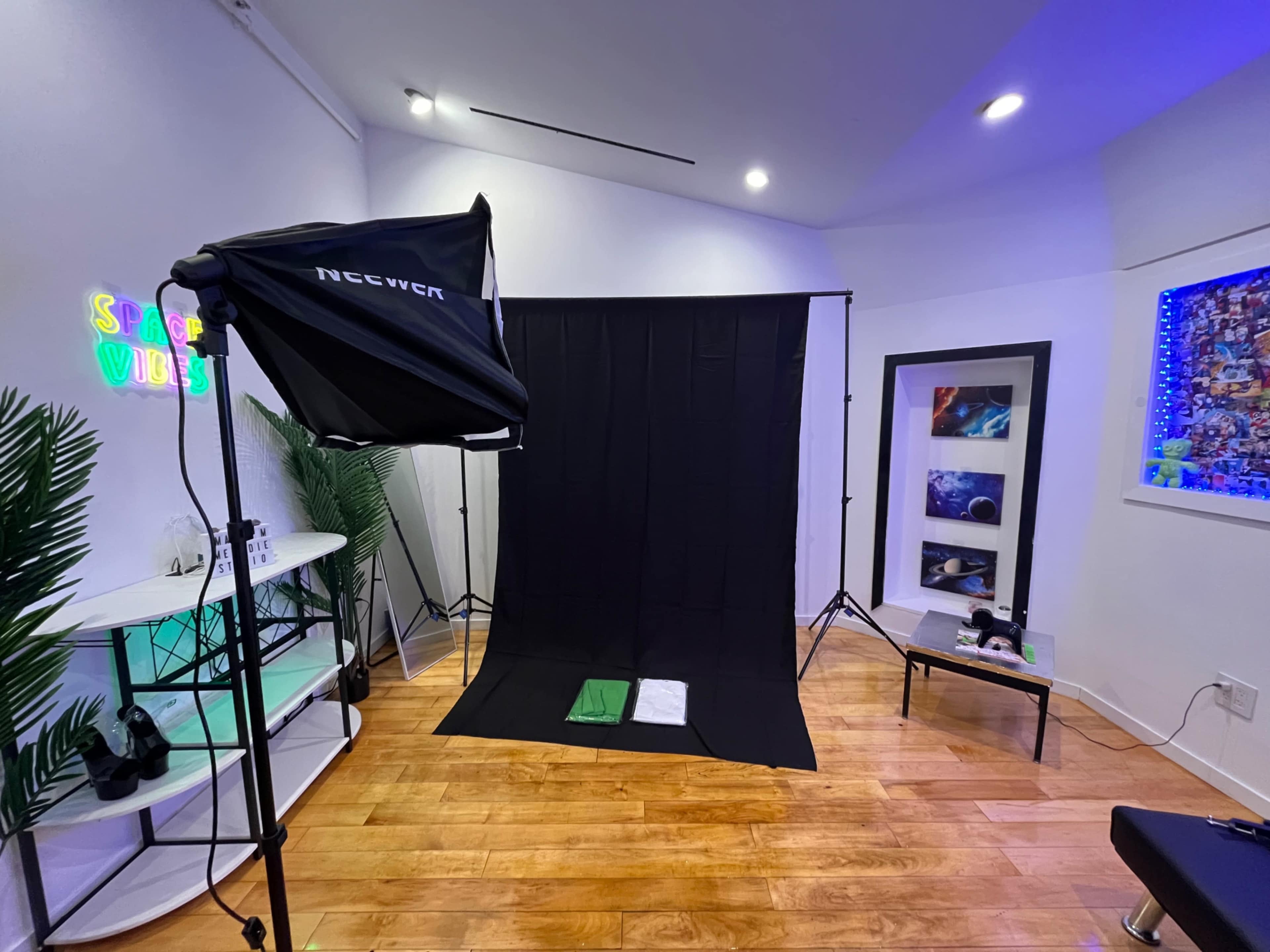 A photography studio setup with a black backdrop, a lighting softbox, and various props arranged on a nearby table.