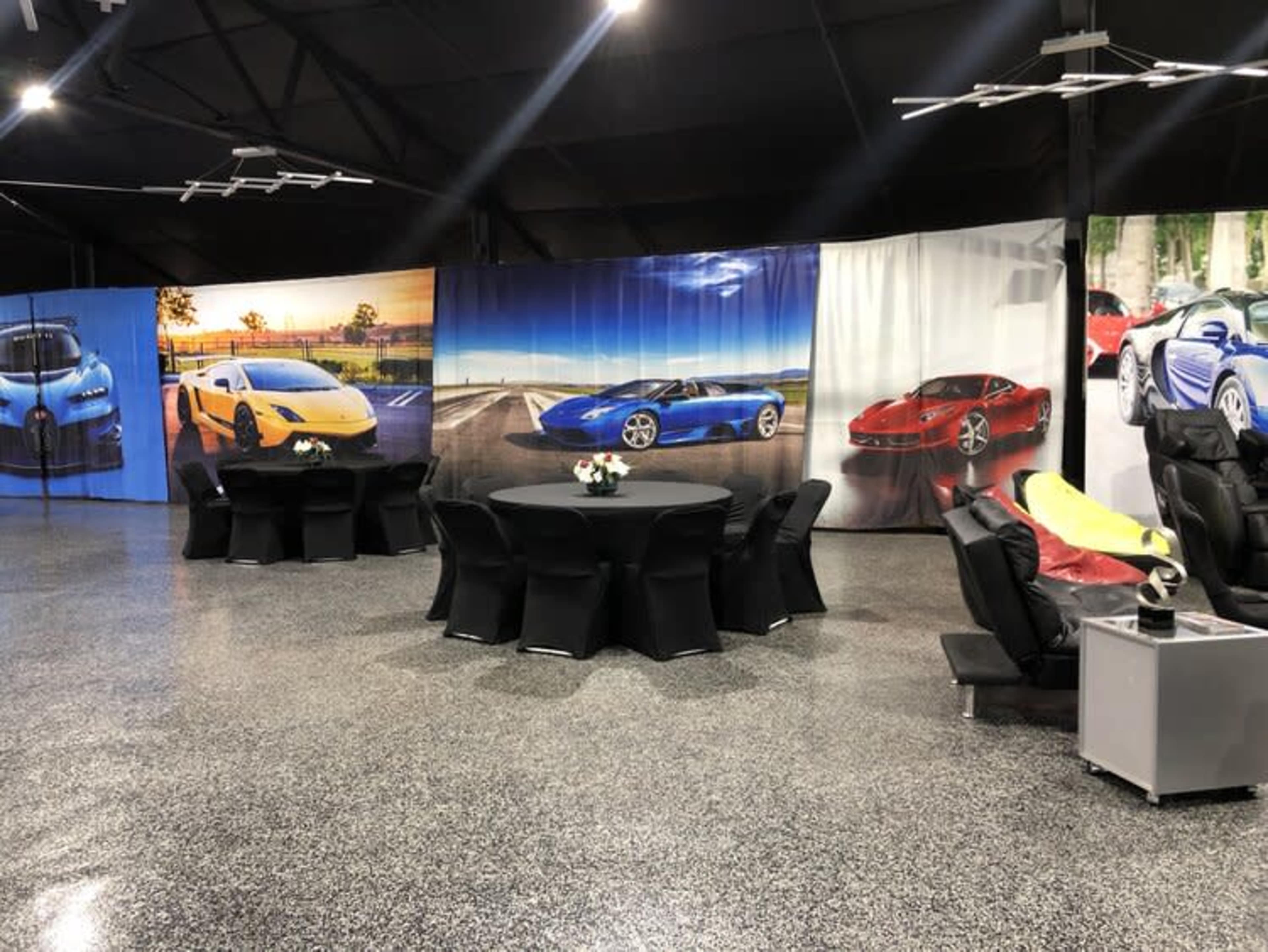 A room with a circular table surrounded by chairs, featuring large, colorful car-themed wall displays.