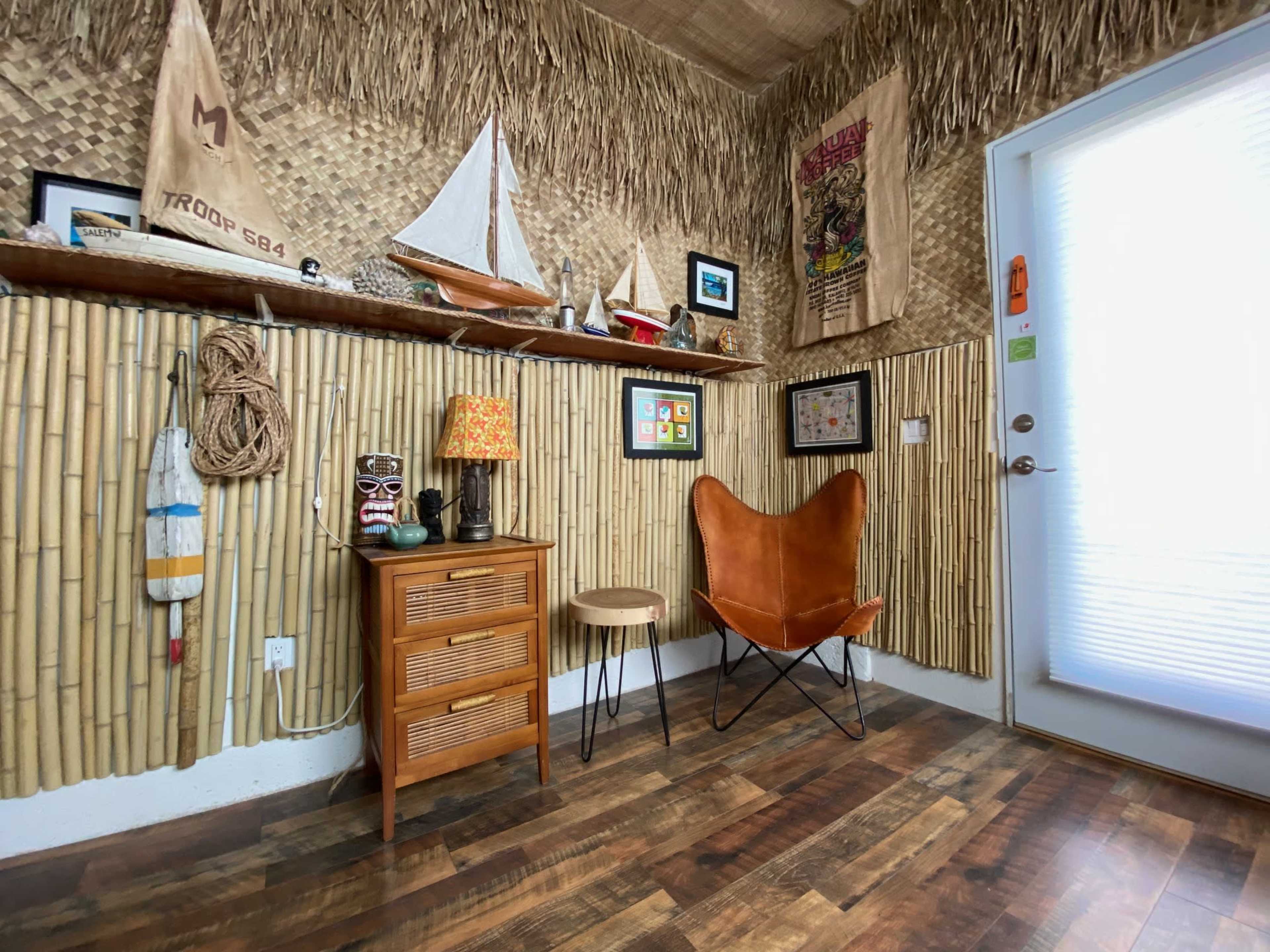 A small corner of a room decorated with bamboo walls, featuring a wooden shelf with decorative items, a butterfly chair, and a small table with a lamp.