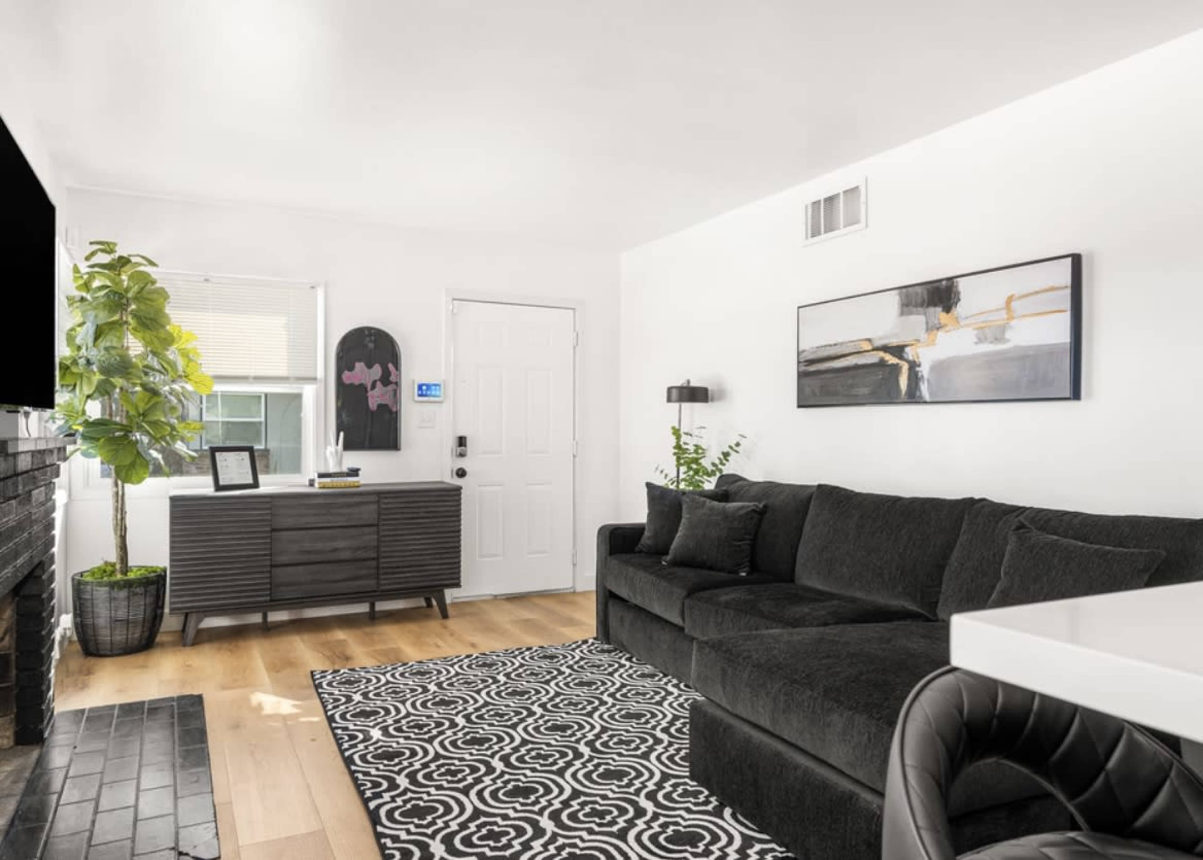 A modern living room features a dark sectional sofa, a black and white patterned rug, a console table, and a door leading outside.
