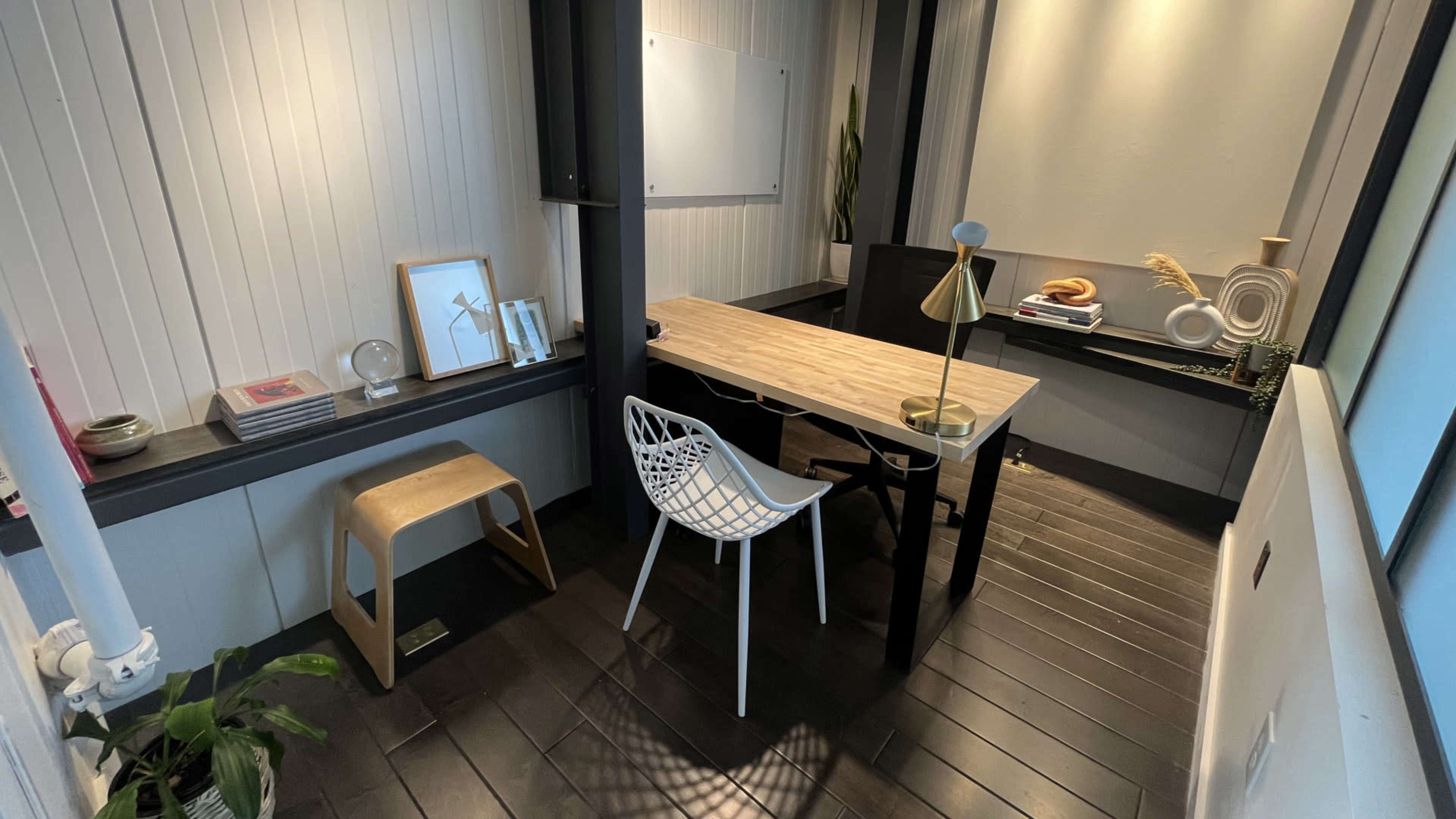 A modern, minimalist office space with a wooden table, a white chair, and decorative elements on the walls and surfaces.