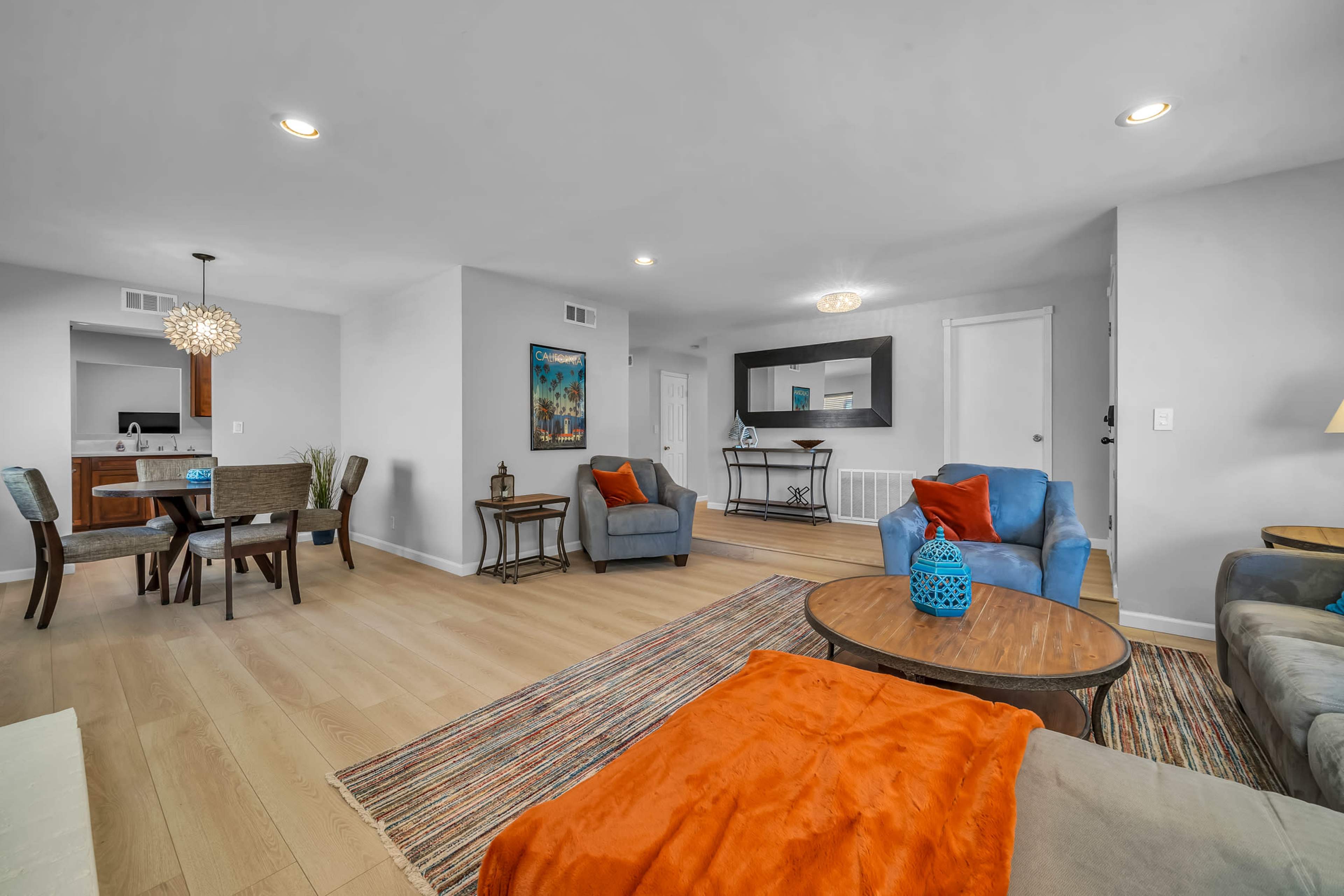 The image shows a modern living room with a mix of seating options, a coffee table, and a dining area in the background.