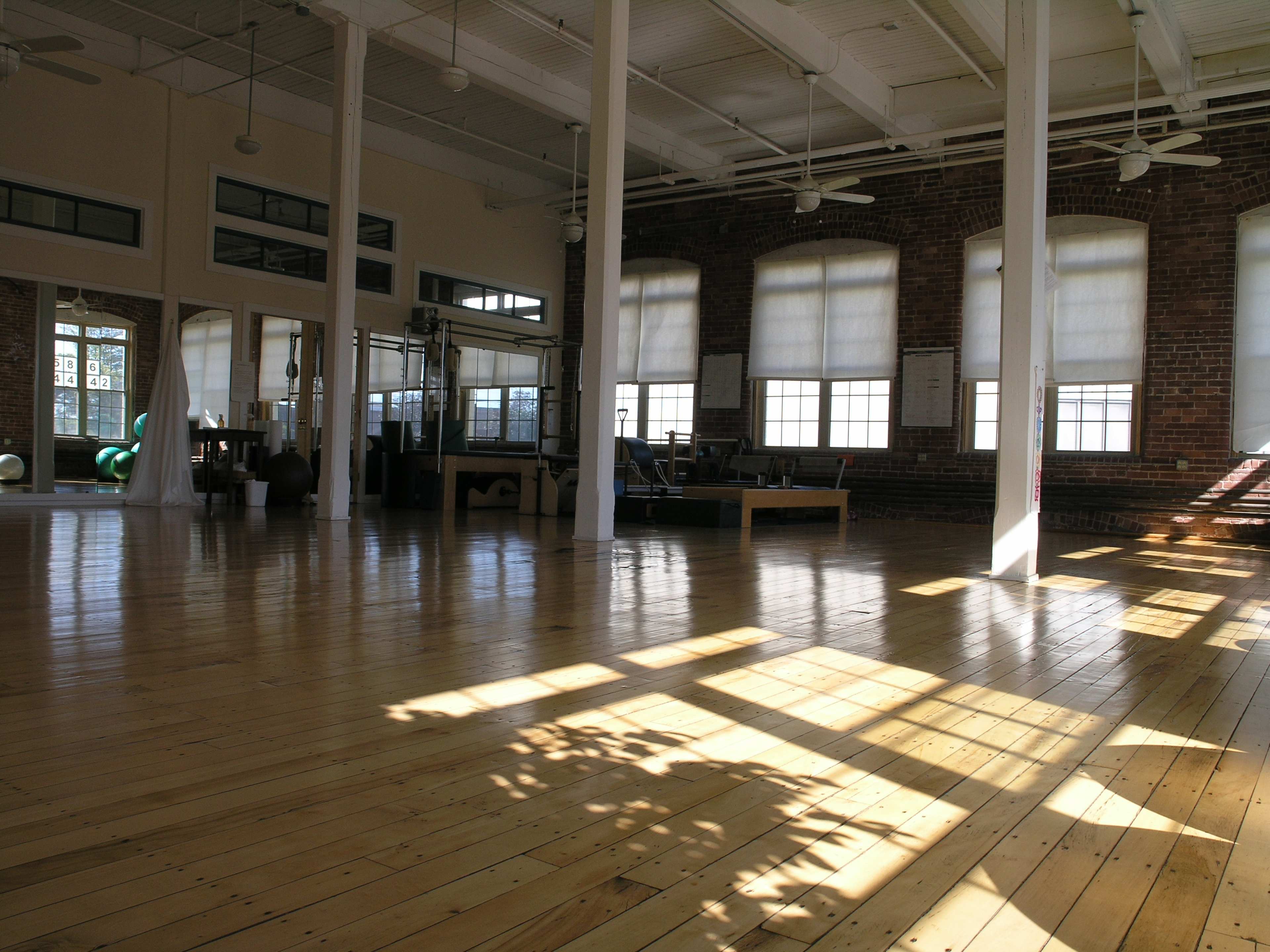 A spacious, well-lit studio with wooden floors and large windows, featuring exercise equipment in the background.