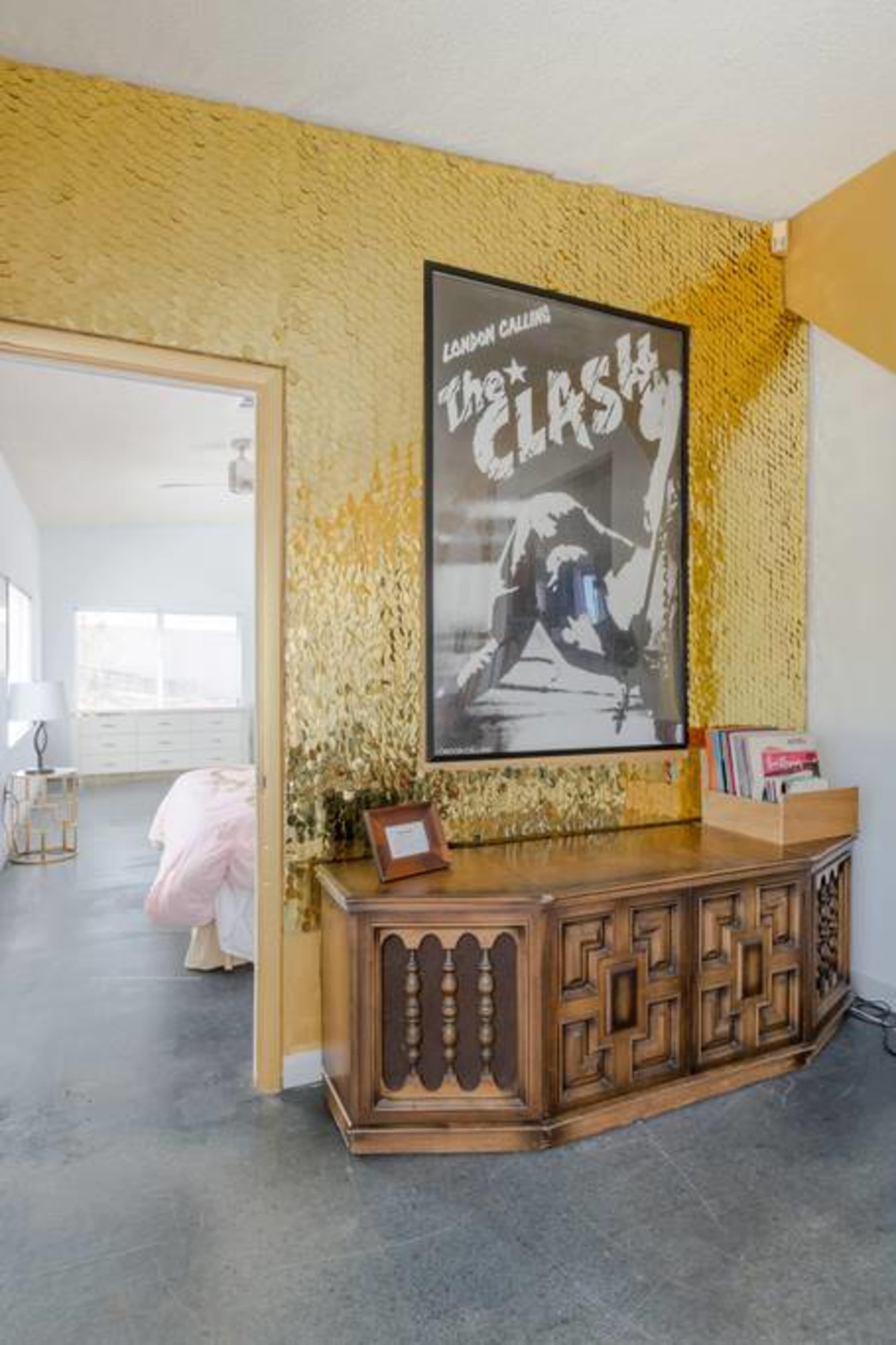 A hallway with a gold-textured wall and a wooden console table displaying a framed poster and magazines.