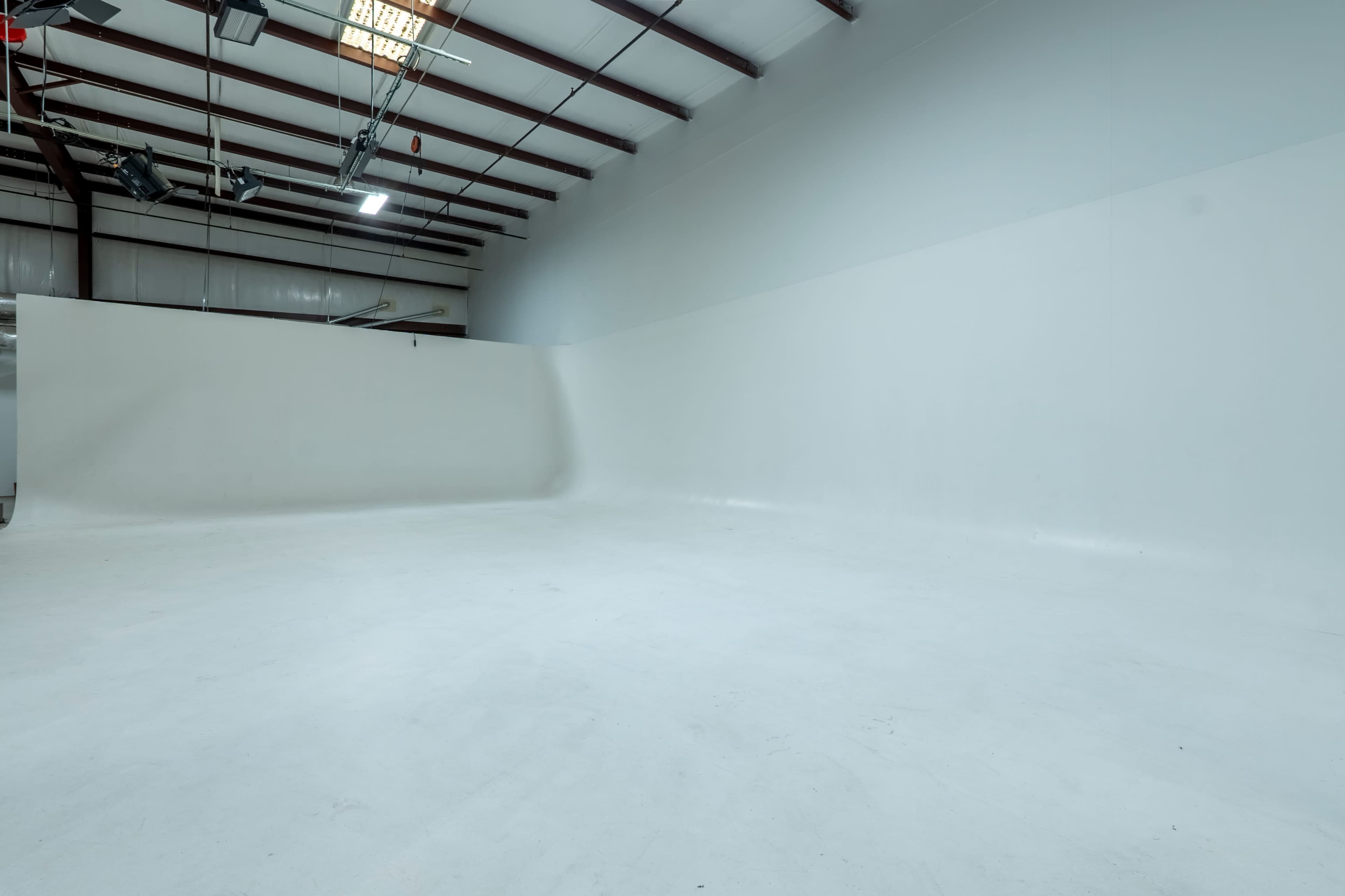 The image shows a spacious, empty studio with white walls and a smooth floor under a metal roof.
