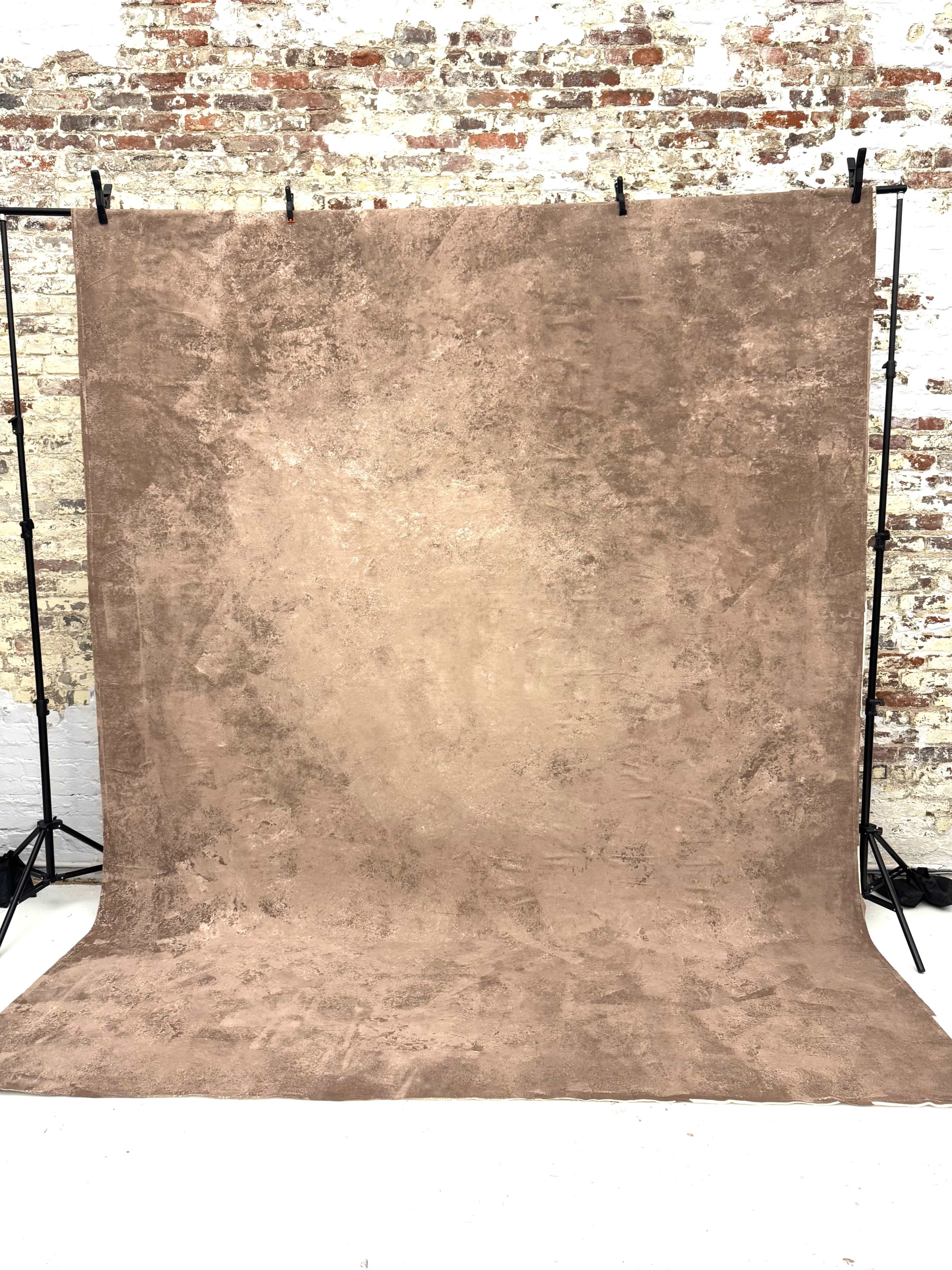 The image shows a textured, brown backdrop positioned against a brick wall, supported by black stands.