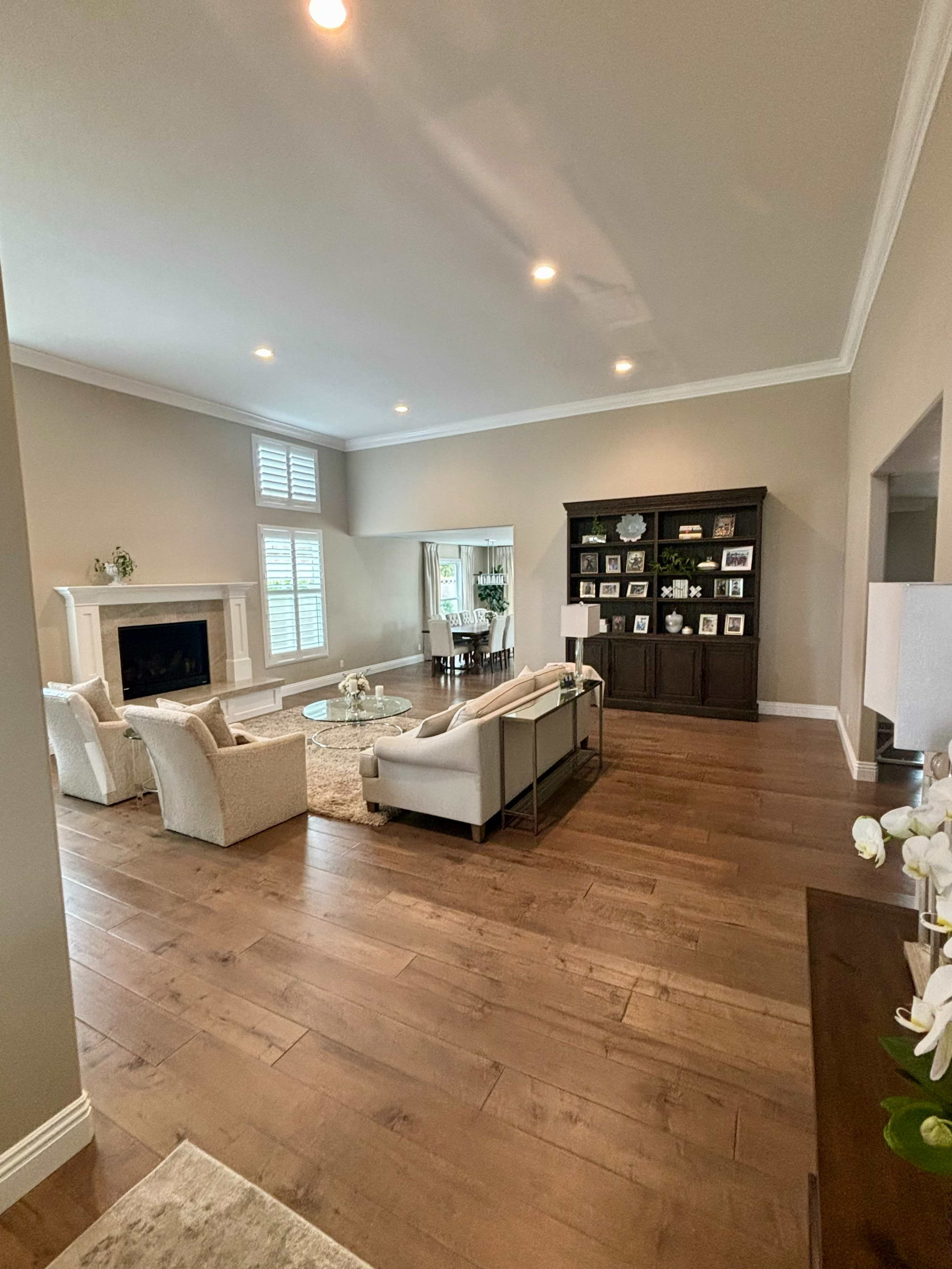 A spacious living room featuring a fireplace, a coffee table, and a dark wooden cabinet with framed photos.