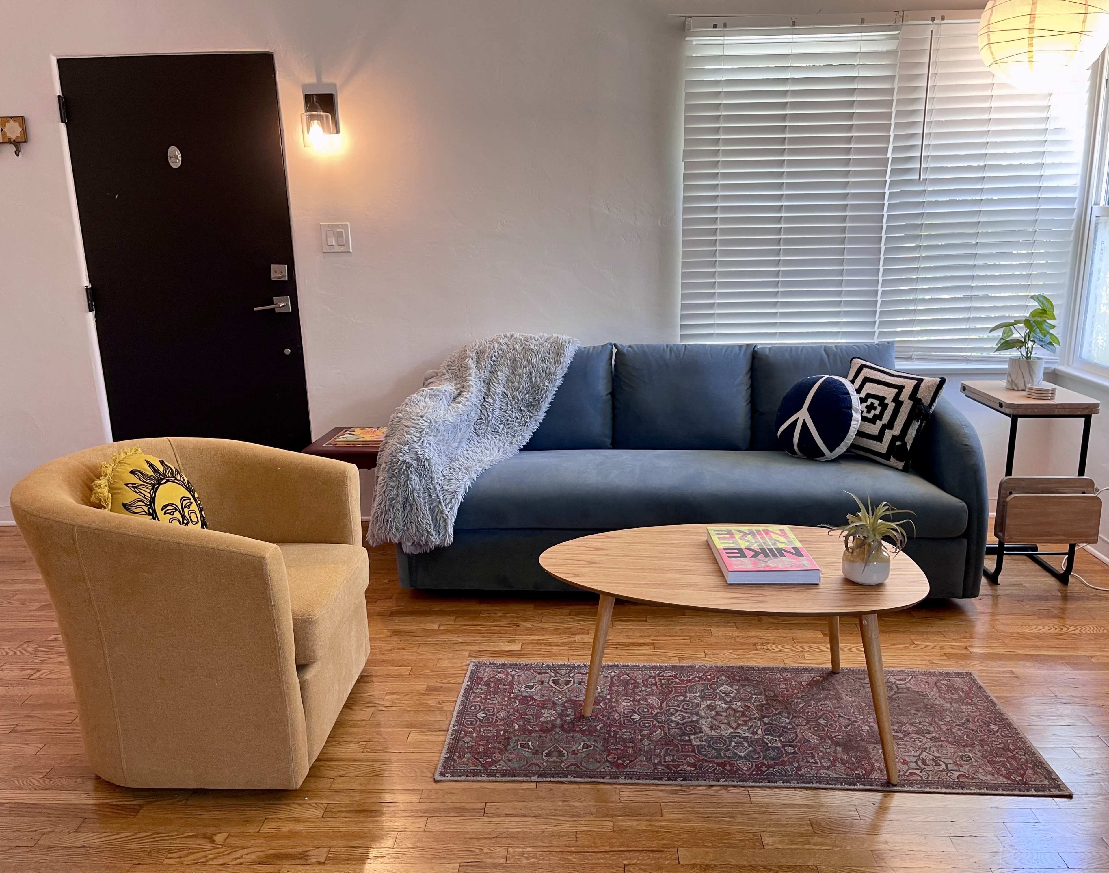 A living room with a blue couch, a yellow armchair, a coffee table, and a window displaying natural light.