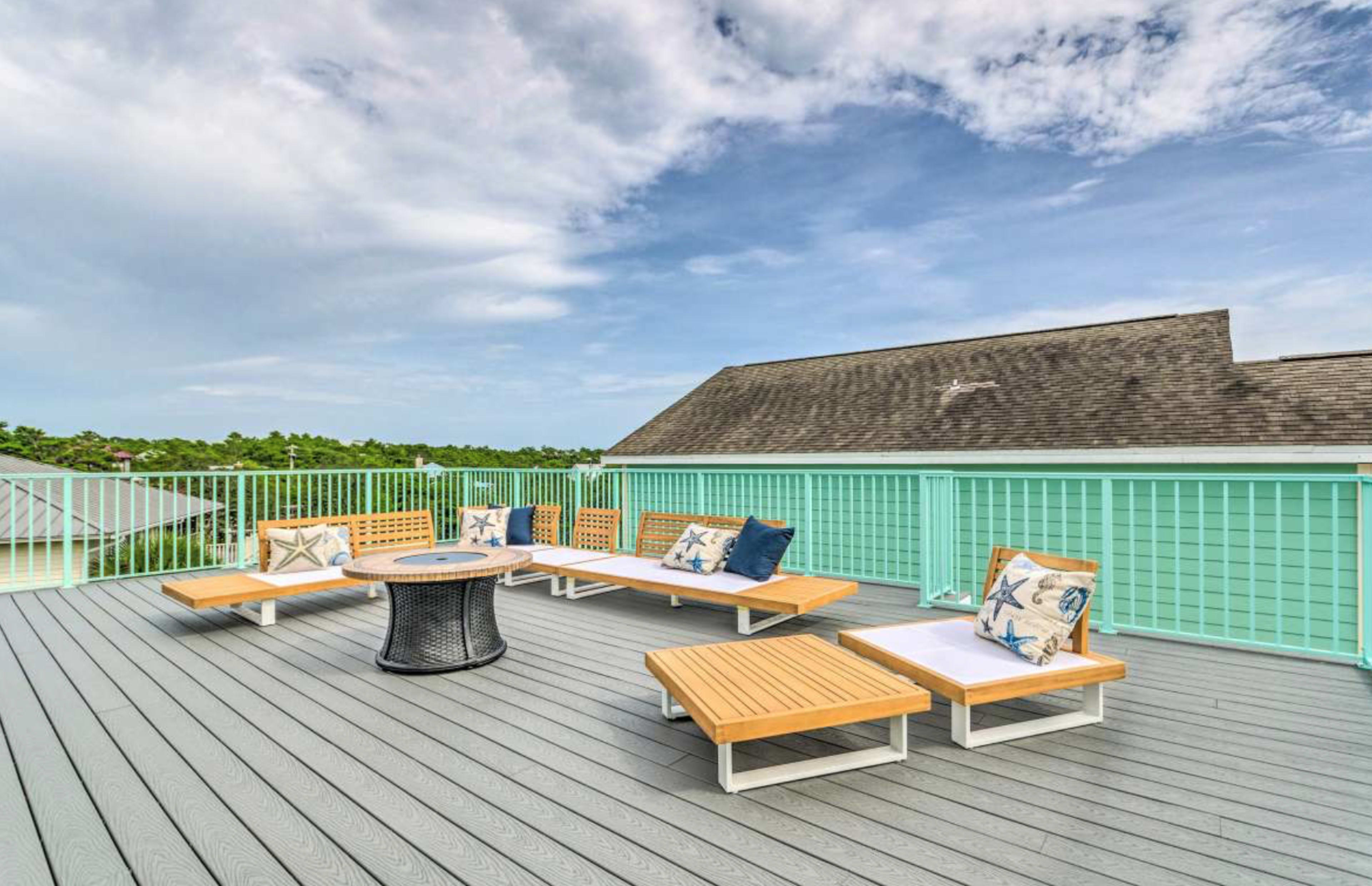 A deck features wooden lounge furniture and a circular table, overlooking a green landscape under a partly cloudy sky.