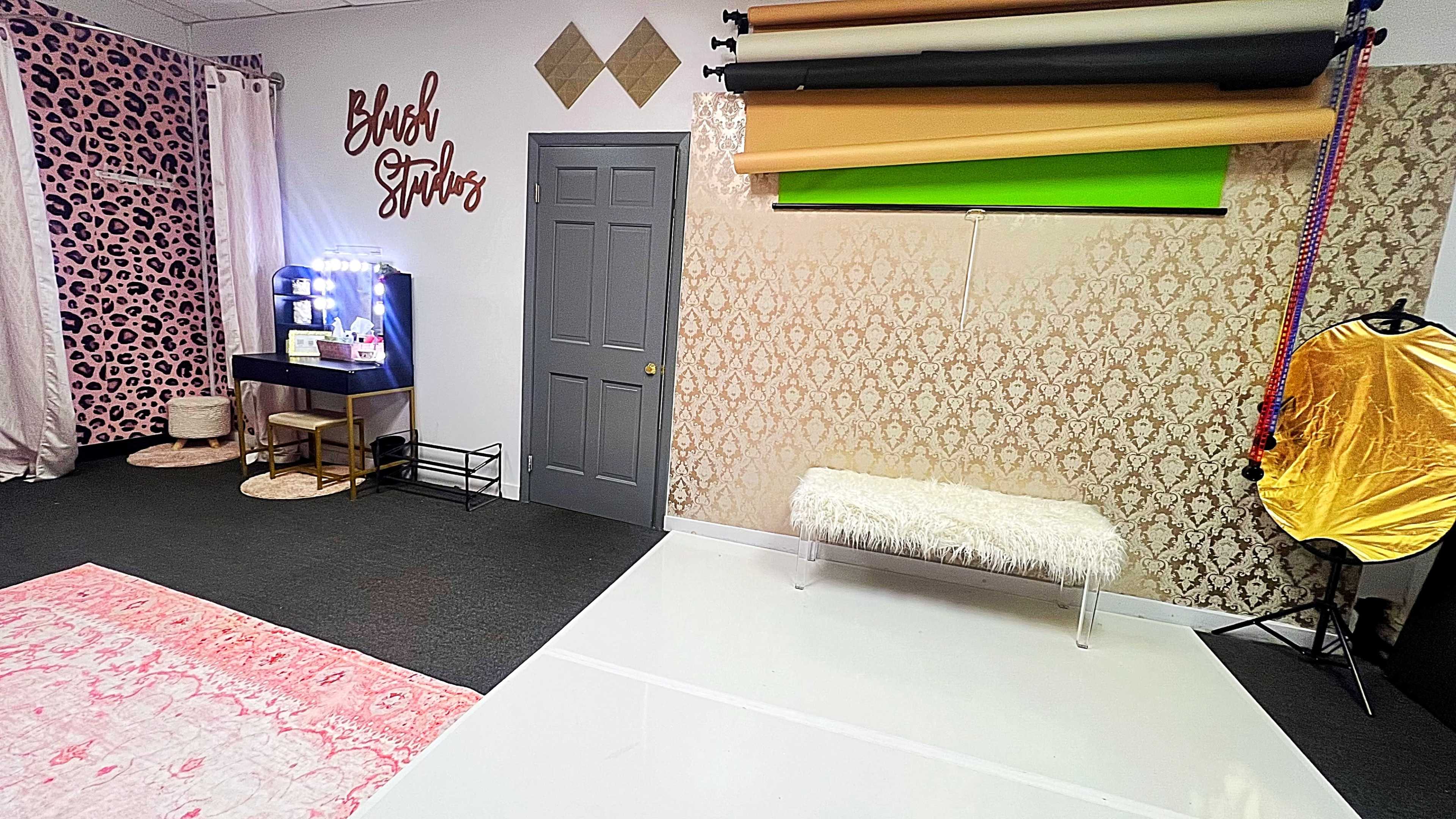 The image shows a photography studio with a variety of backdrops, a vanity station with lights, and a white floor space.