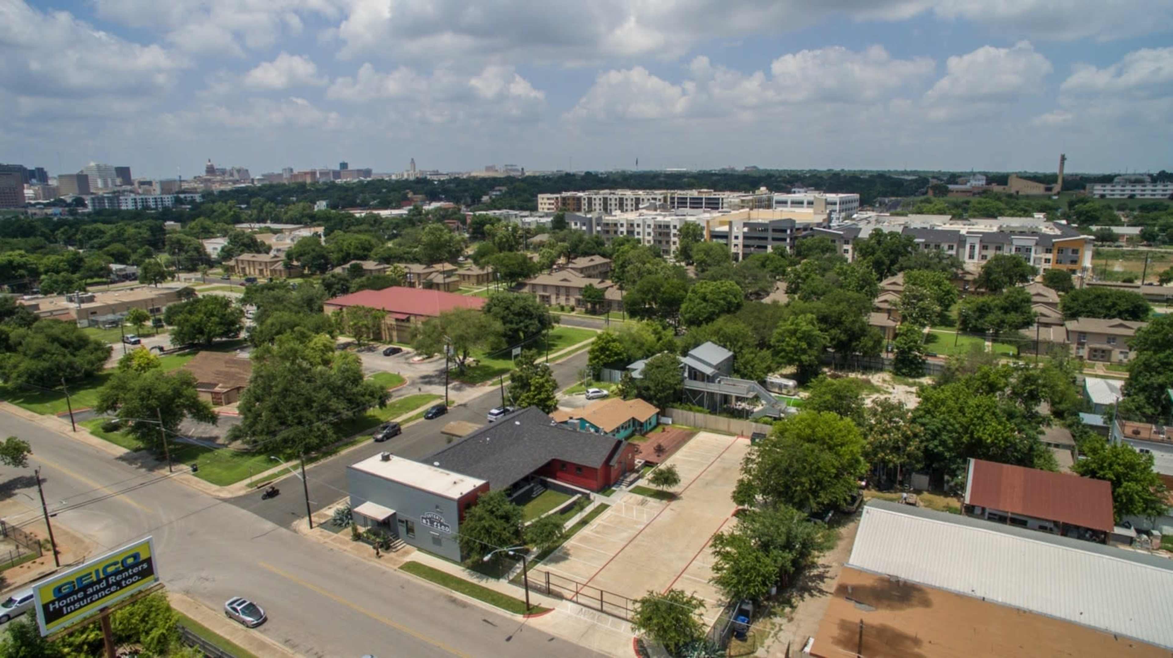 The image shows an aerial view of a suburban area featuring residential buildings, green trees, and a mix of commercial establishments.
