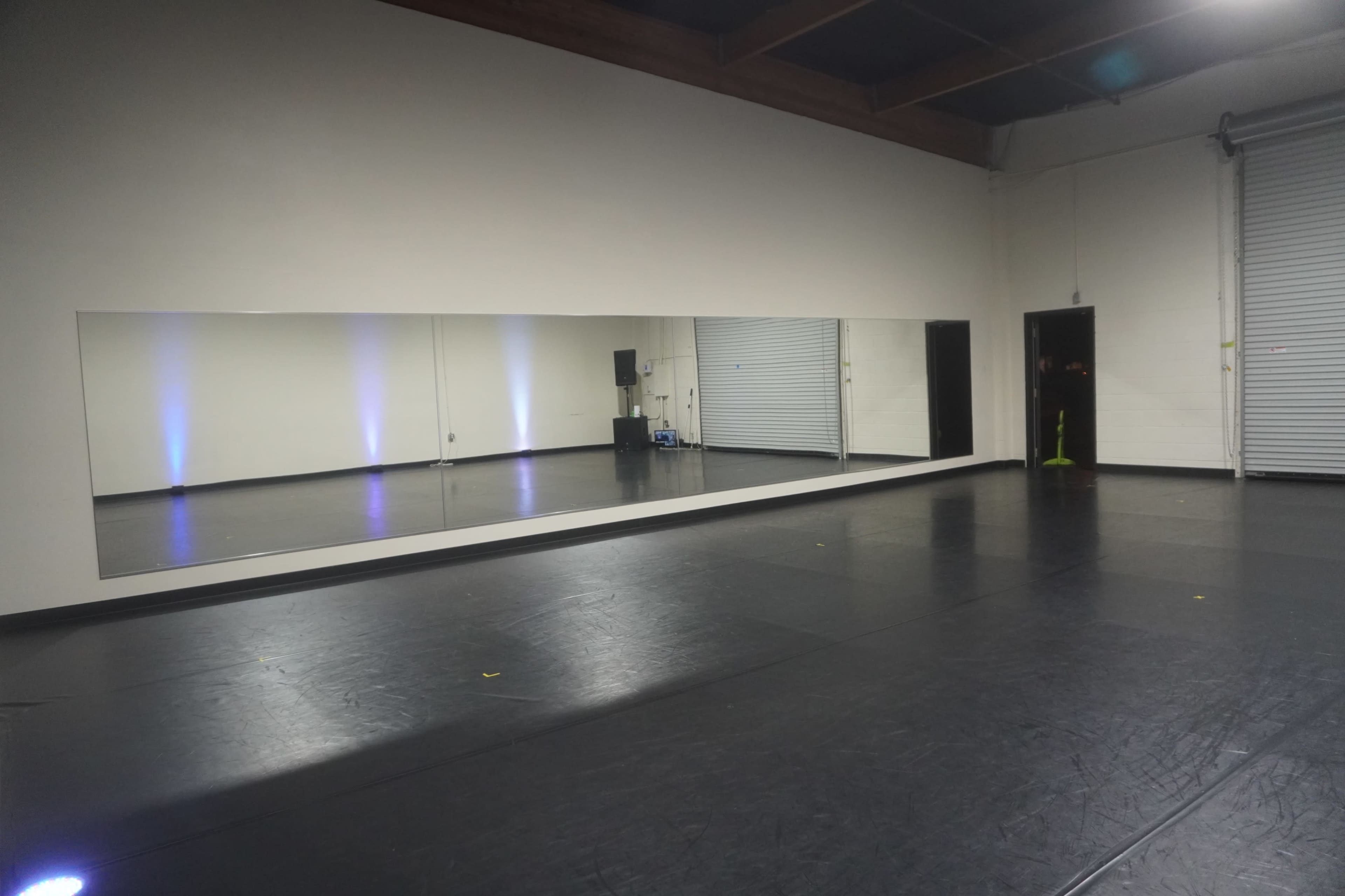 A spacious dance studio with a long mirror along one wall and black flooring.