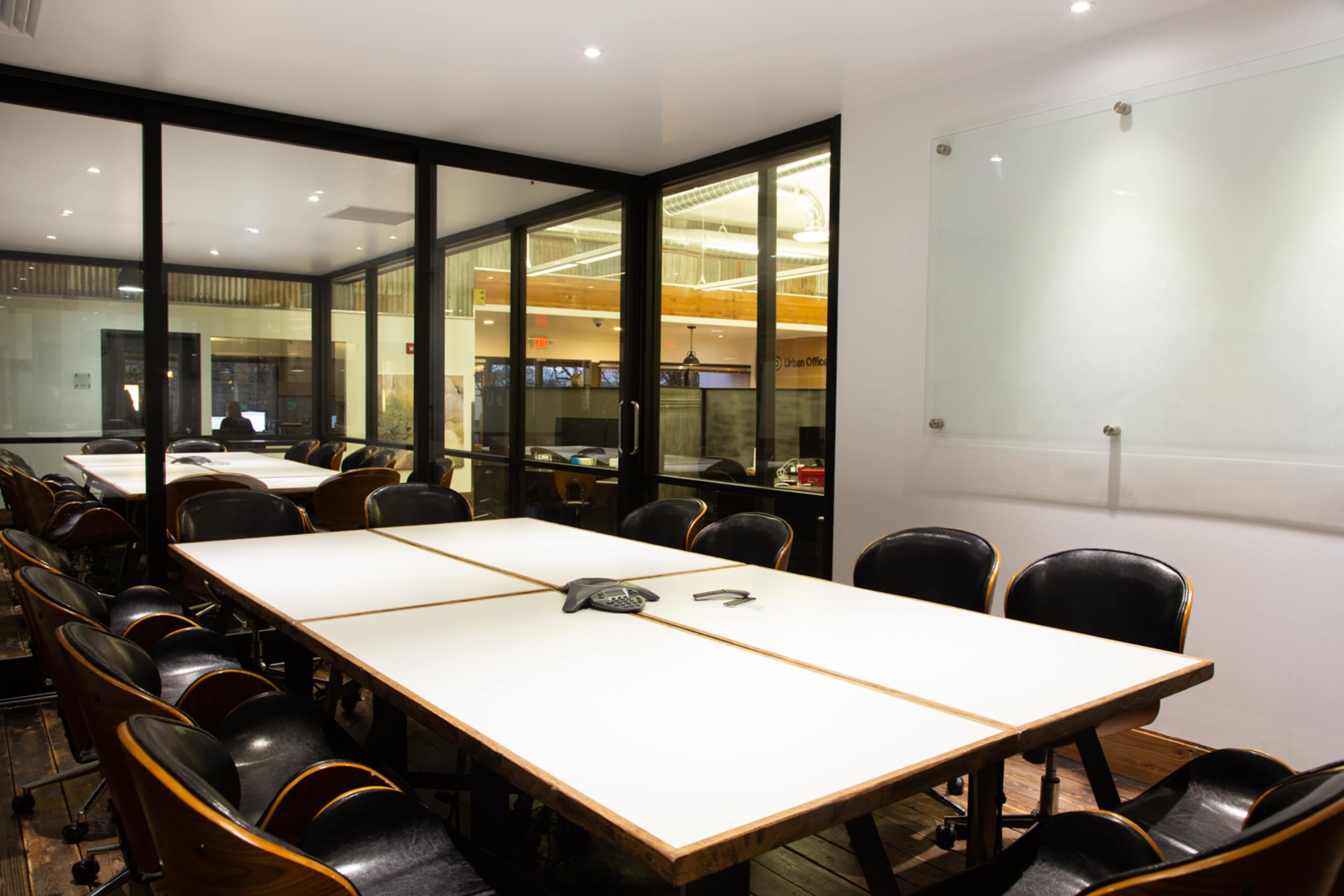 A conference room with a large white table surrounded by black chairs and glass walls.