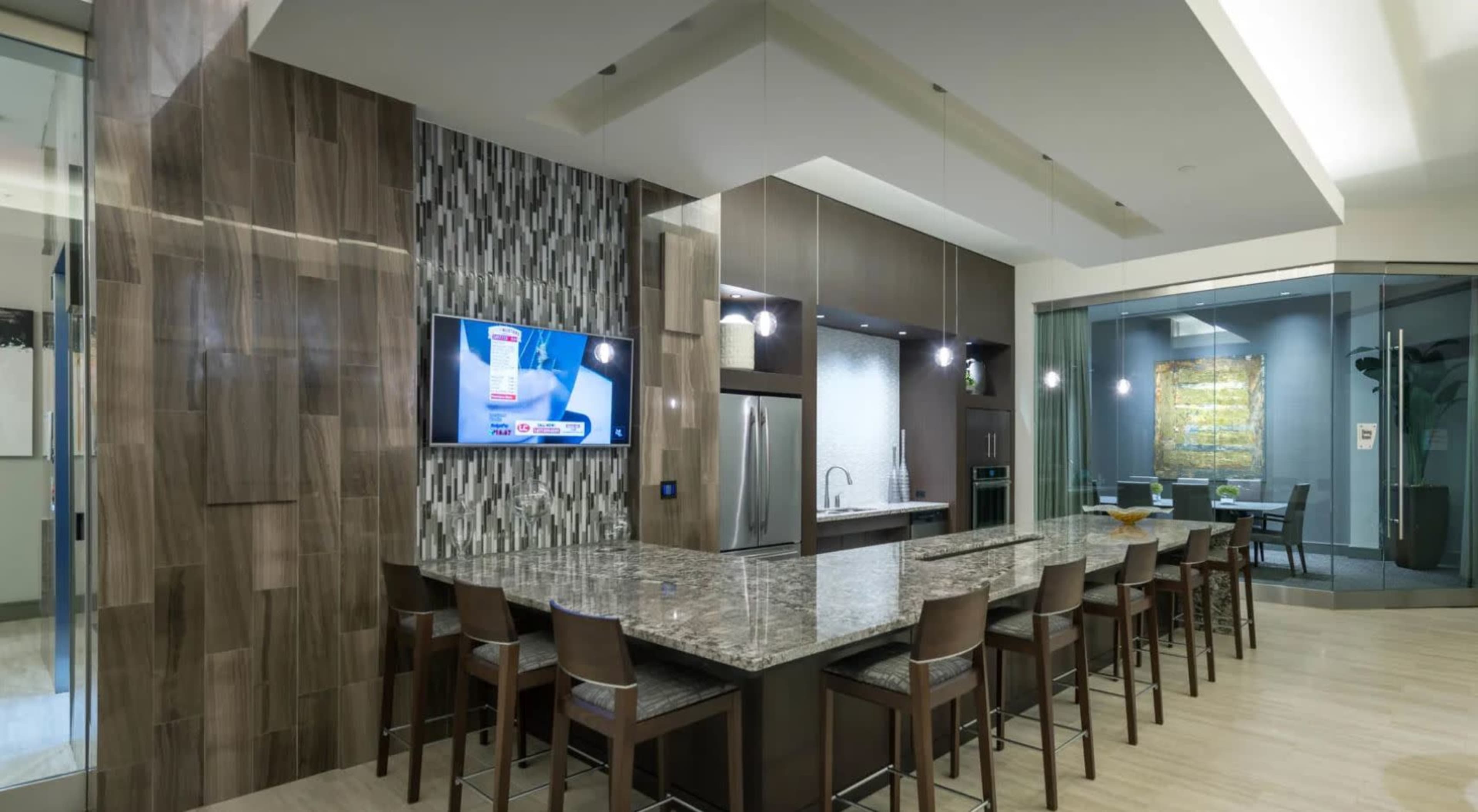 A modern kitchen with a large granite island, a wall-mounted television, and sleek cabinetry.
