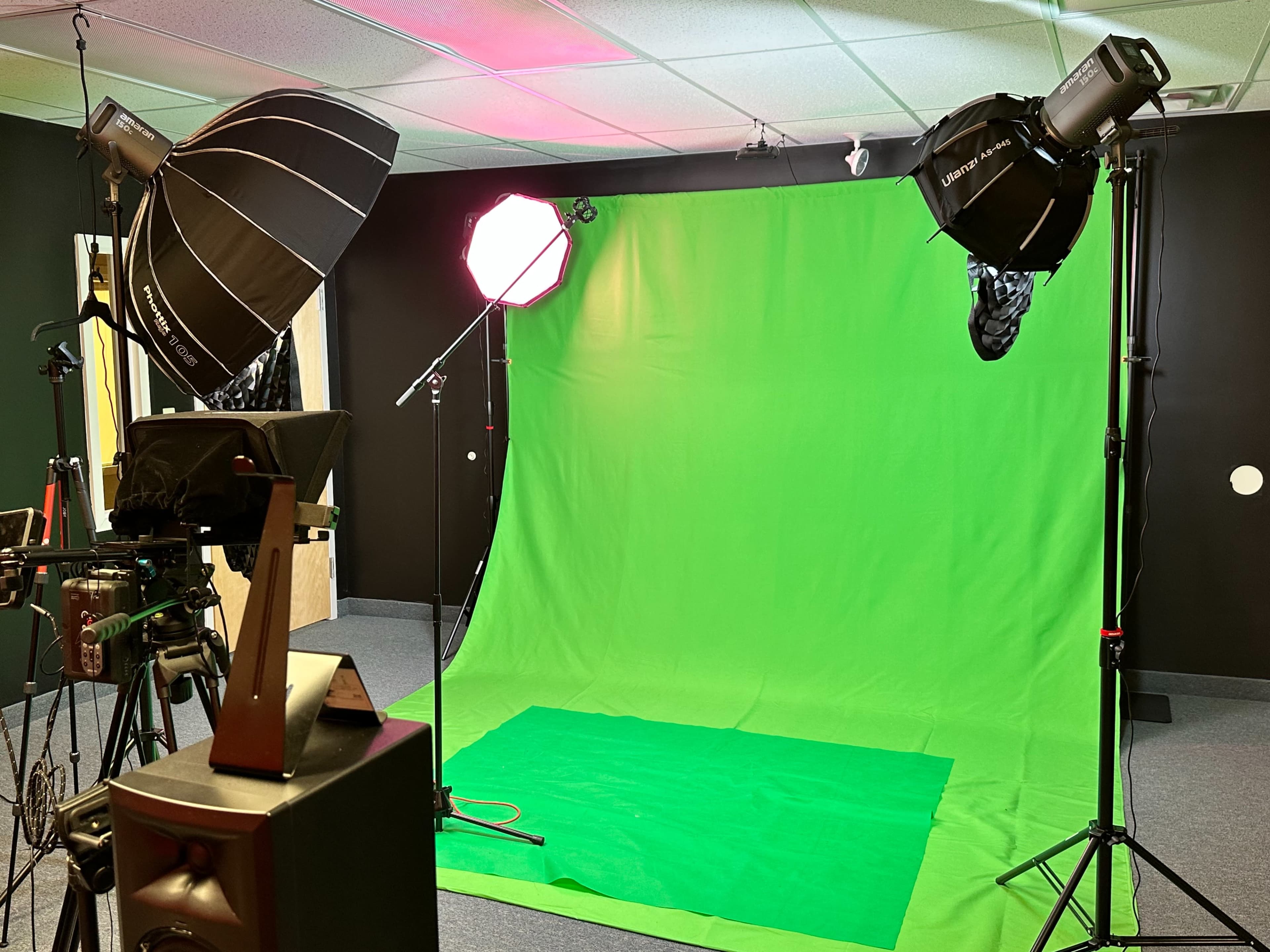 The image shows a green screen setup with multiple light sources and camera equipment in a studio room.