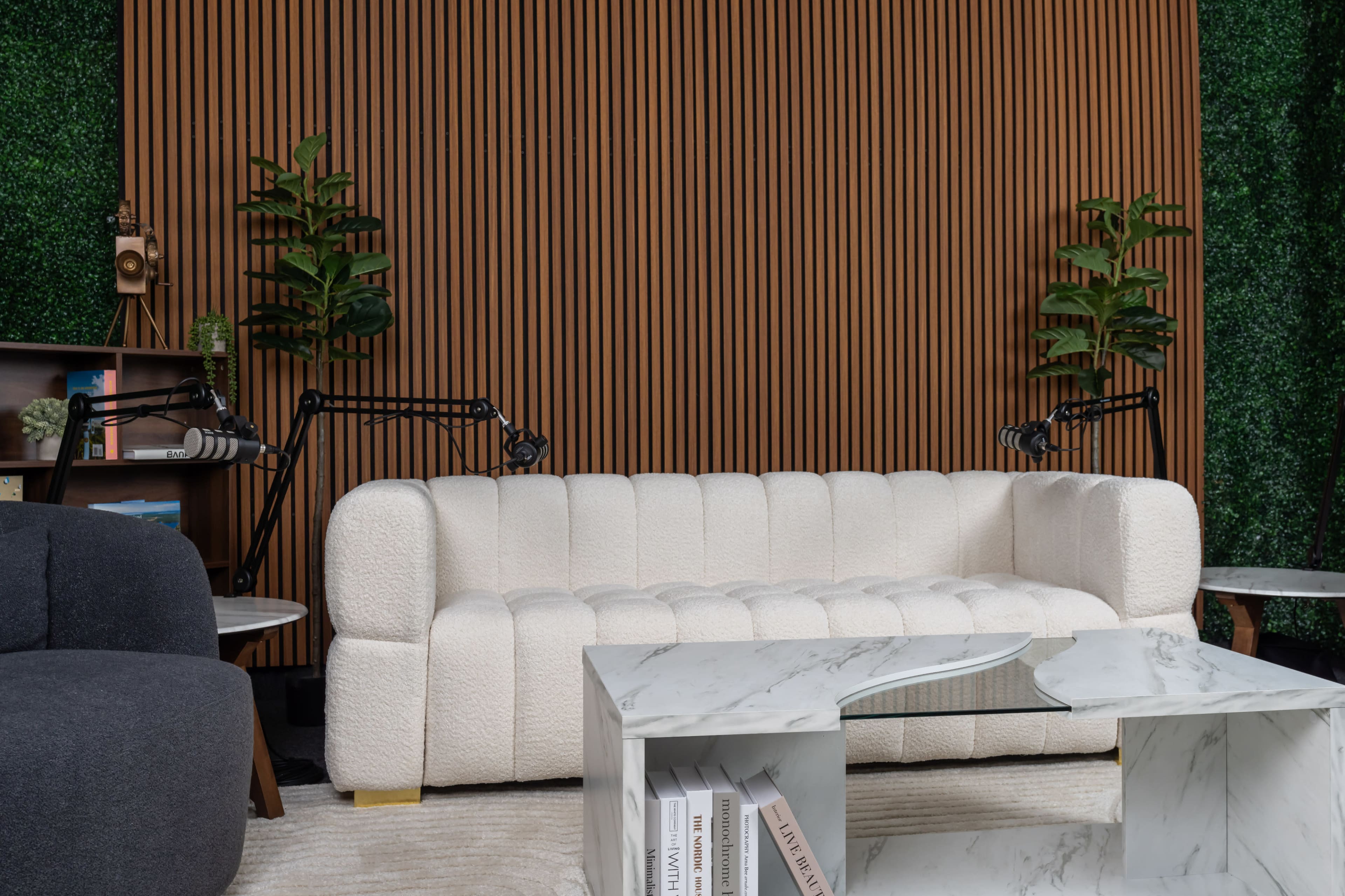 A white, tufted couch sits in front of a wooden slatted wall, accompanied by green plants and modern decor.