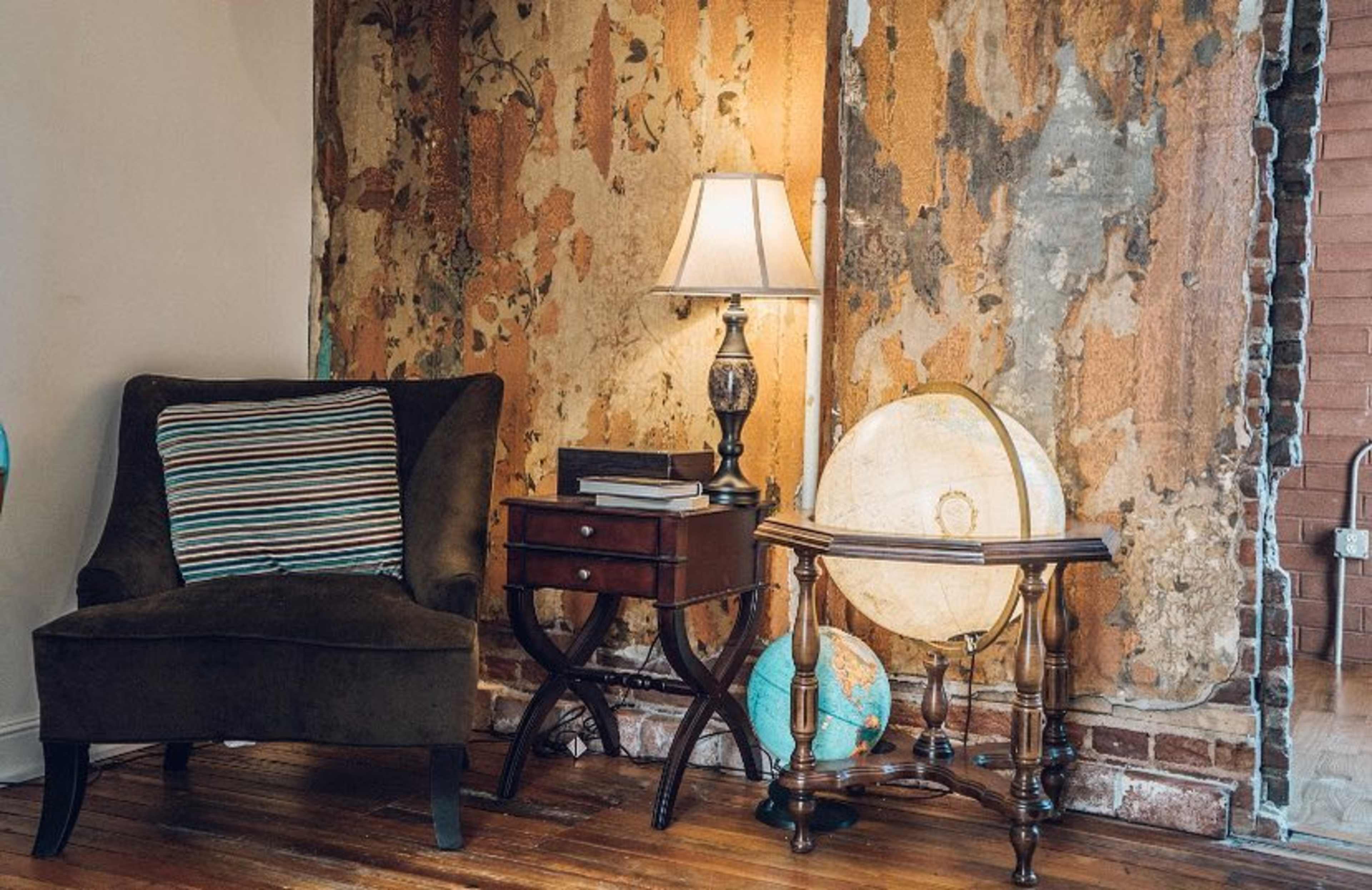 A cozy corner featuring a brown armchair, a lamp on a side table, and a globe beside an exposed, textured wall.