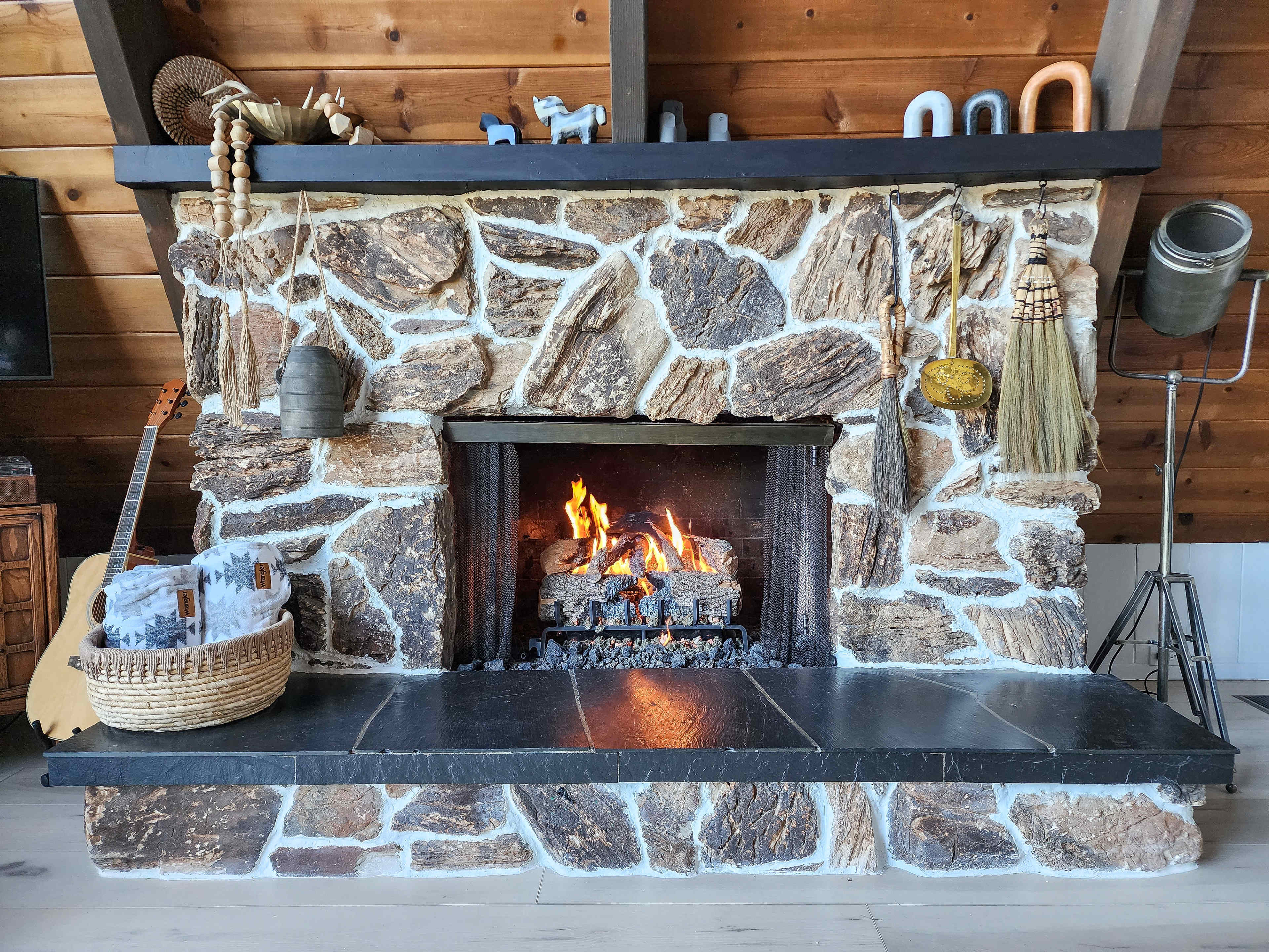 A stone fireplace with a fire burning in the center is surrounded by decorative items and a wooden wall.