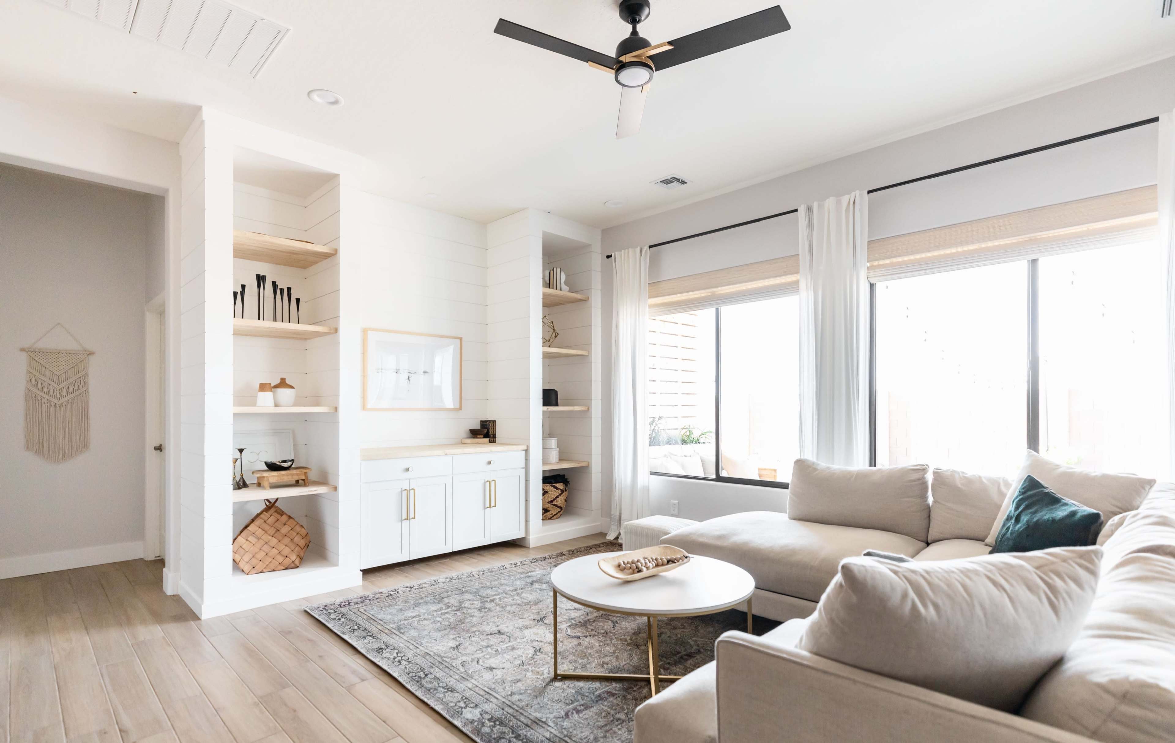 A modern living room featuring a light-colored sectional sofa, a round coffee table, and built-in shelves against a wall.