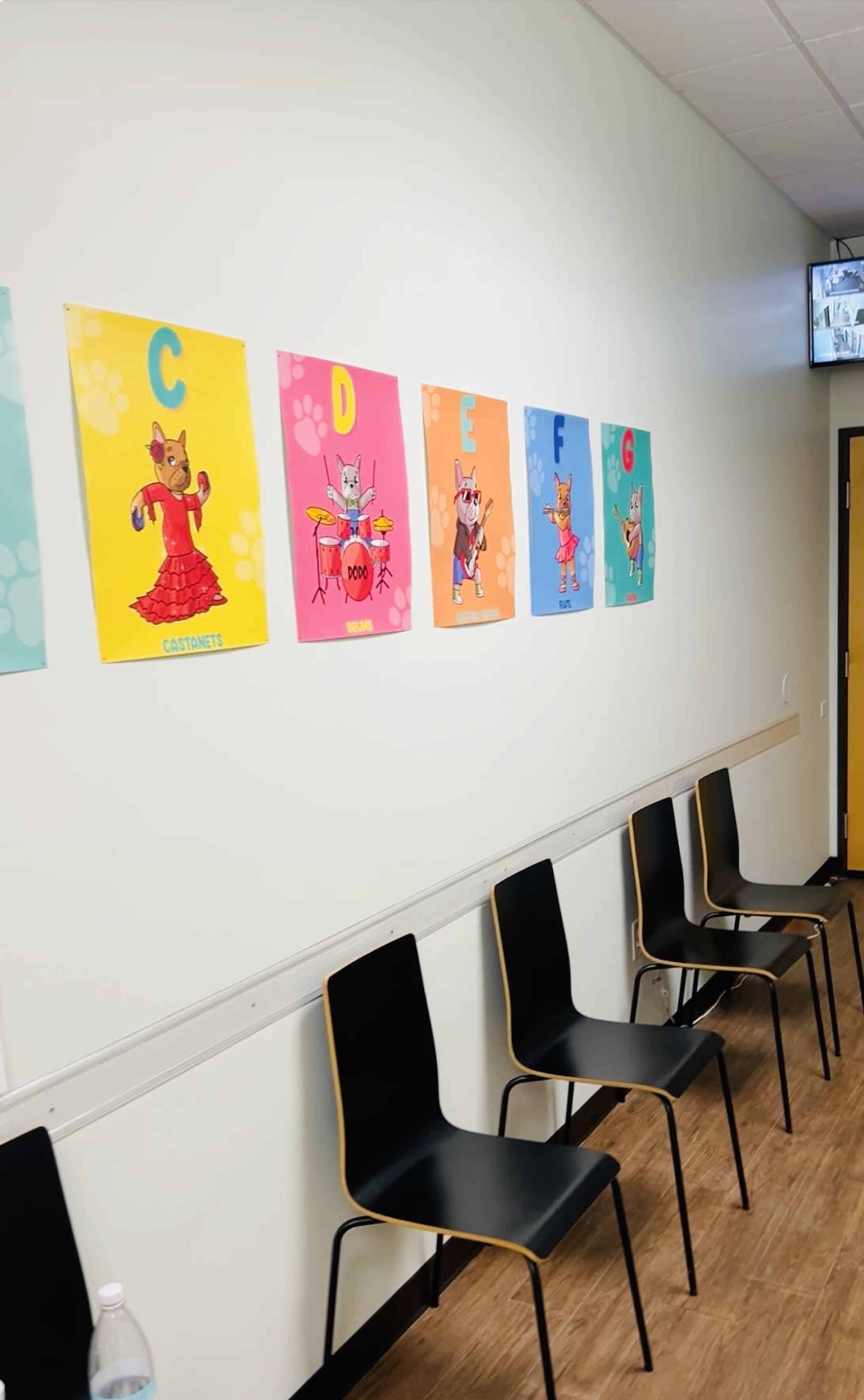 The image shows a white wall with colorful artwork featuring cartoon characters on display, above a row of black chairs.