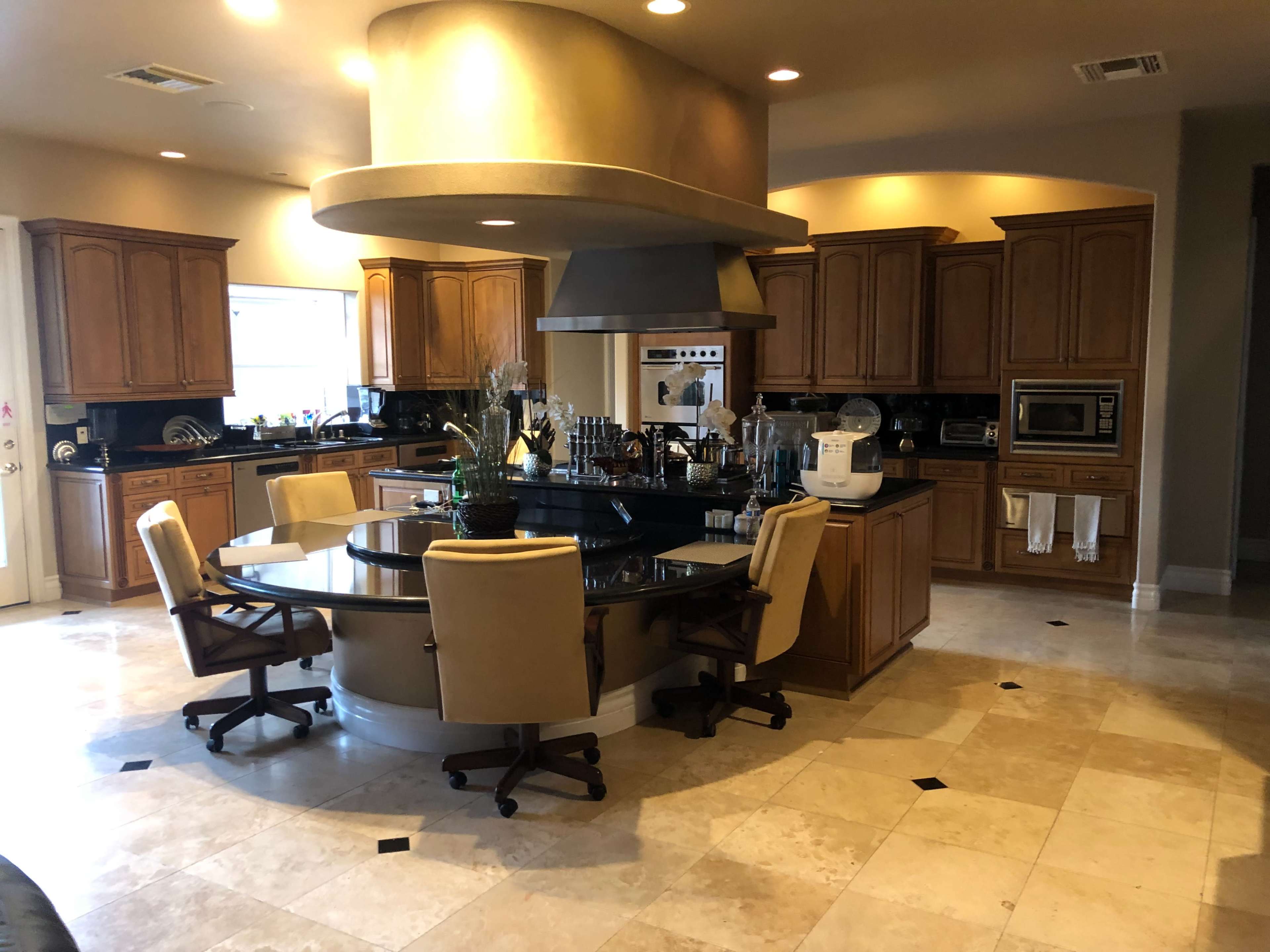 A spacious kitchen with wooden cabinetry, a central circular dining table, and modern appliances.
