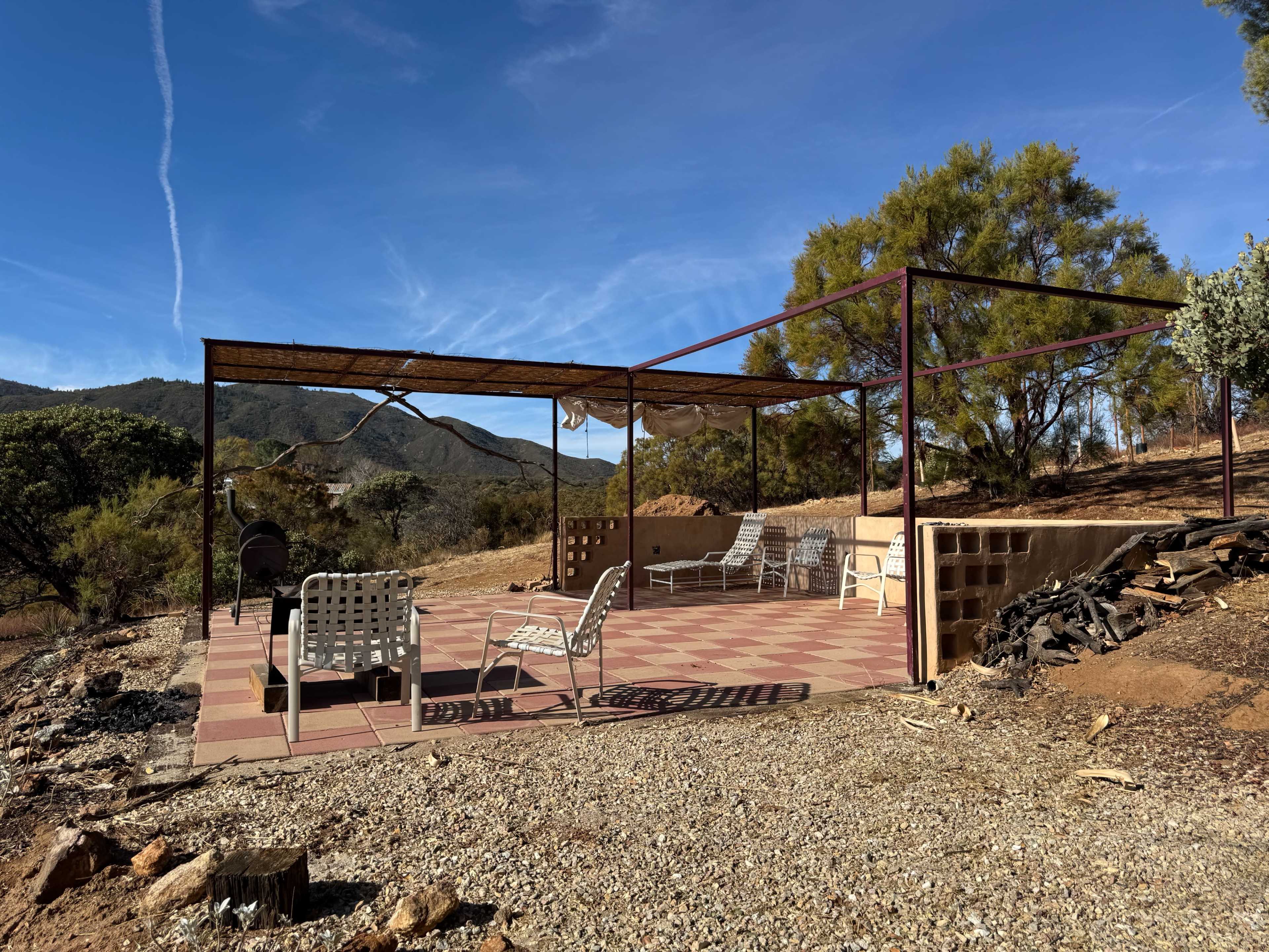 A shaded outdoor patio area features metal-framed seating and a brick floor, surrounded by a mountainous landscape.