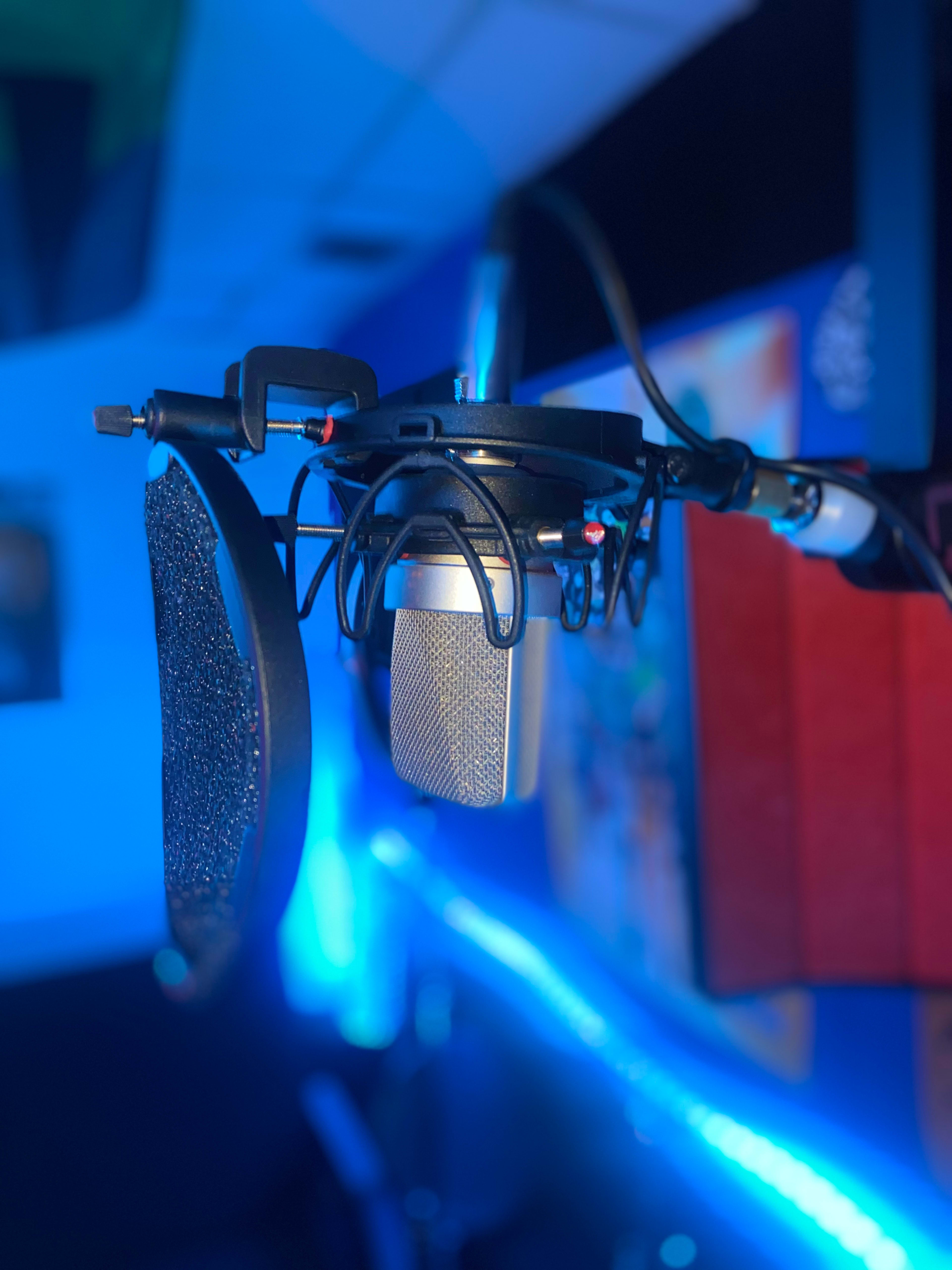 A microphone with a pop filter is suspended from a boom arm in a recording studio.