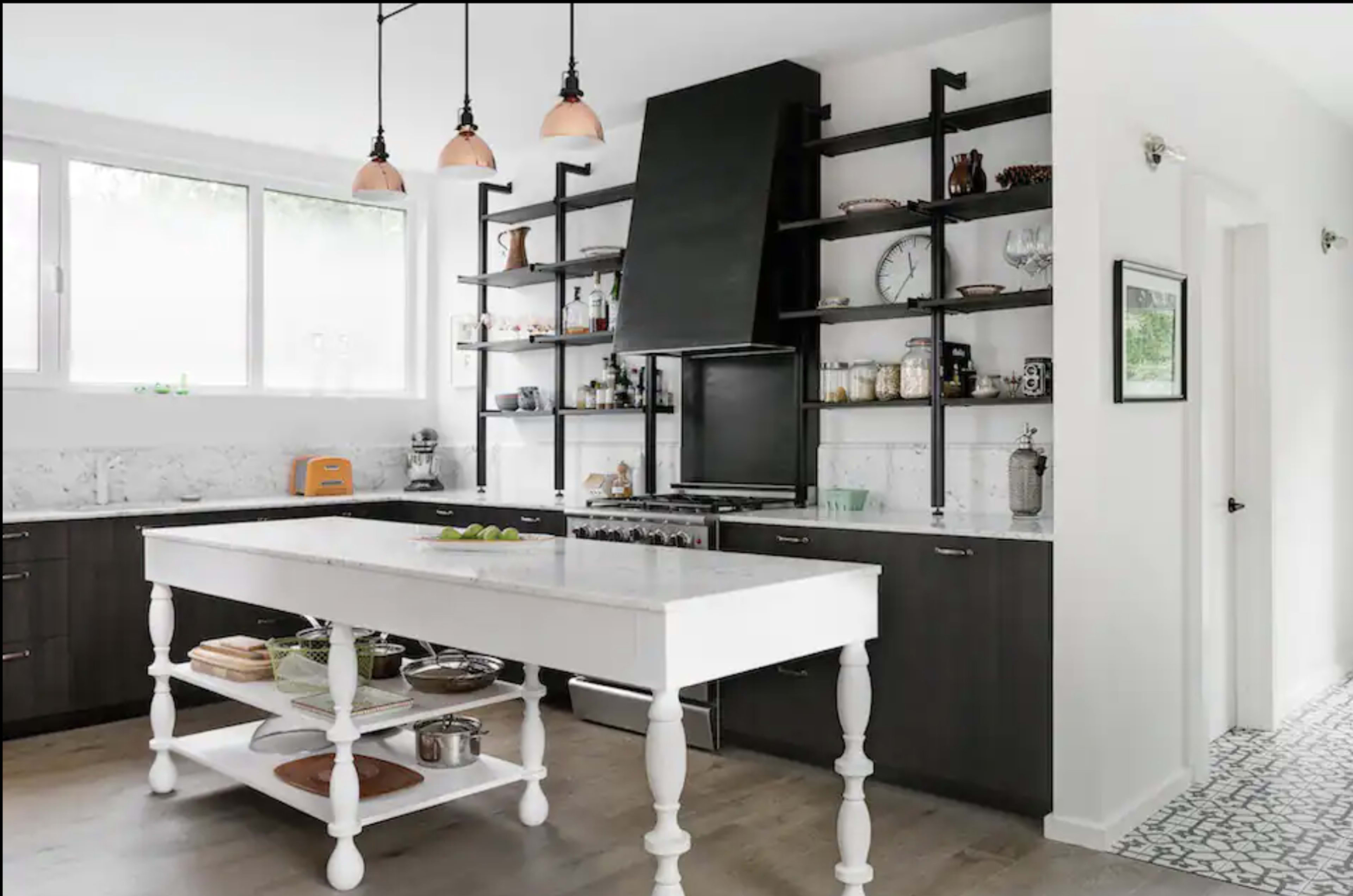 A modern kitchen with dark cabinetry, open shelving, and a central white island with a lower shelf displaying cookware.