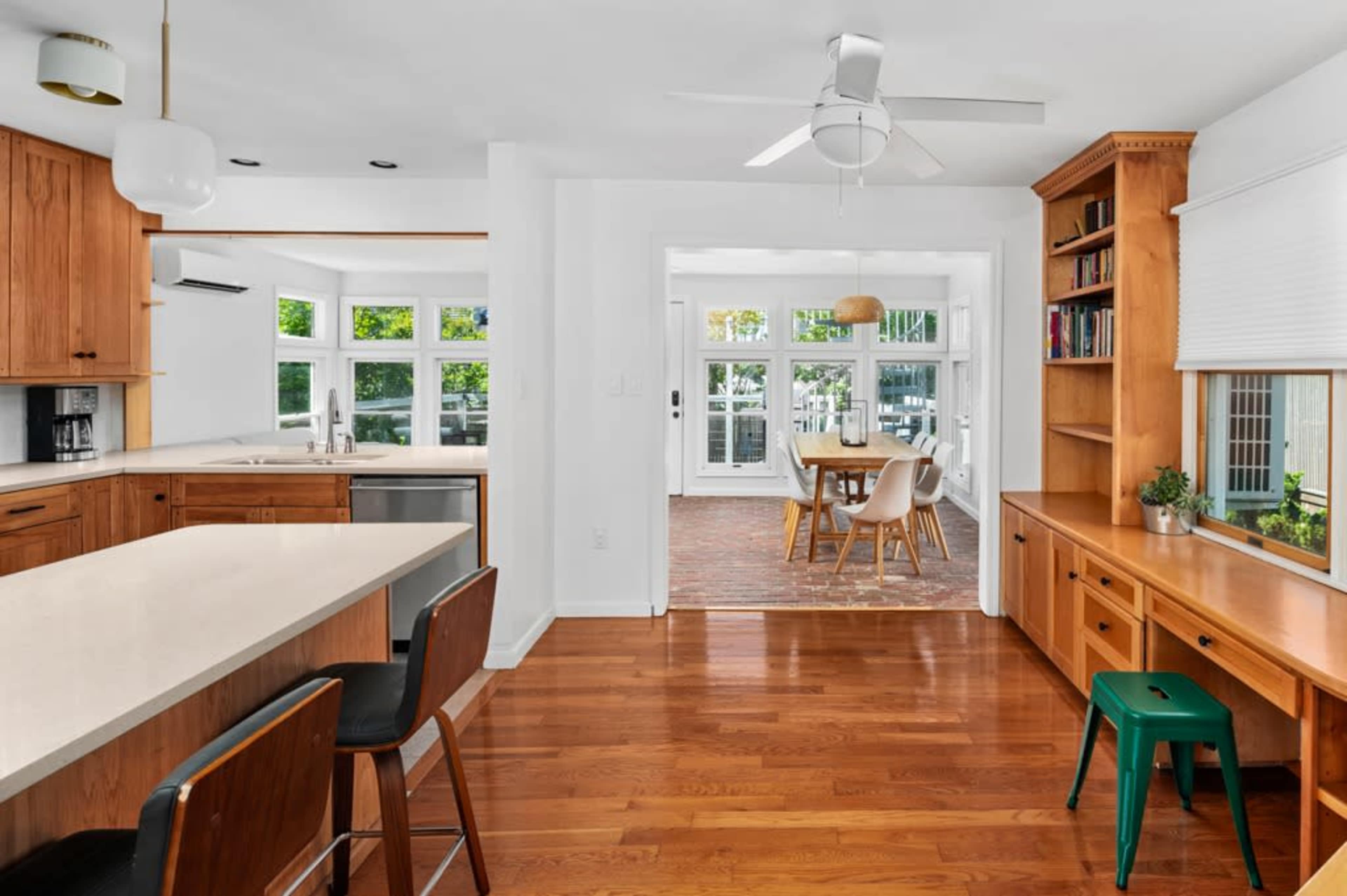 A modern kitchen features wooden cabinets, a large island with seating, and an adjoining sunlit dining area with windows.