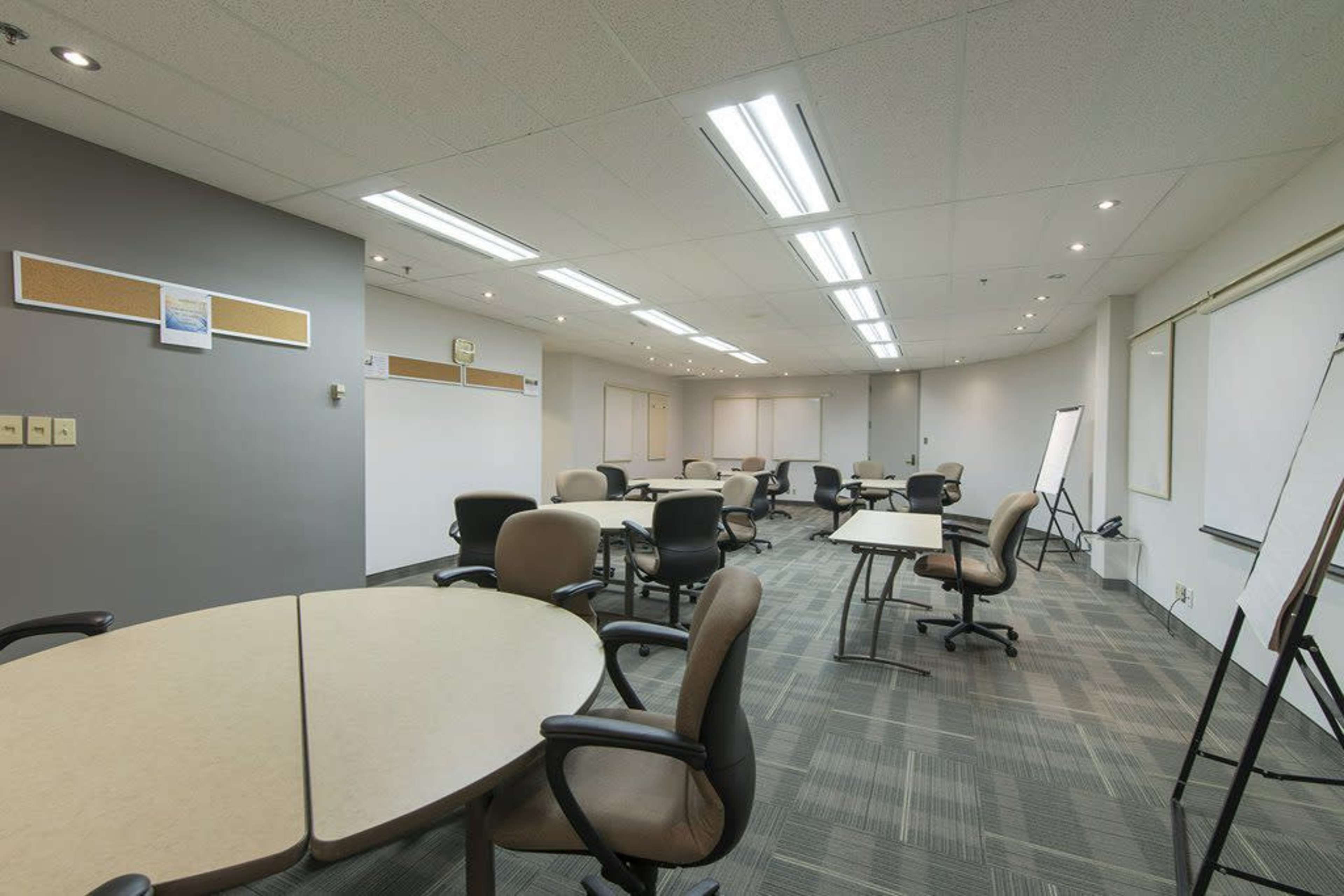 A conference room with multiple round tables and chairs, featuring white walls and overhead lighting.