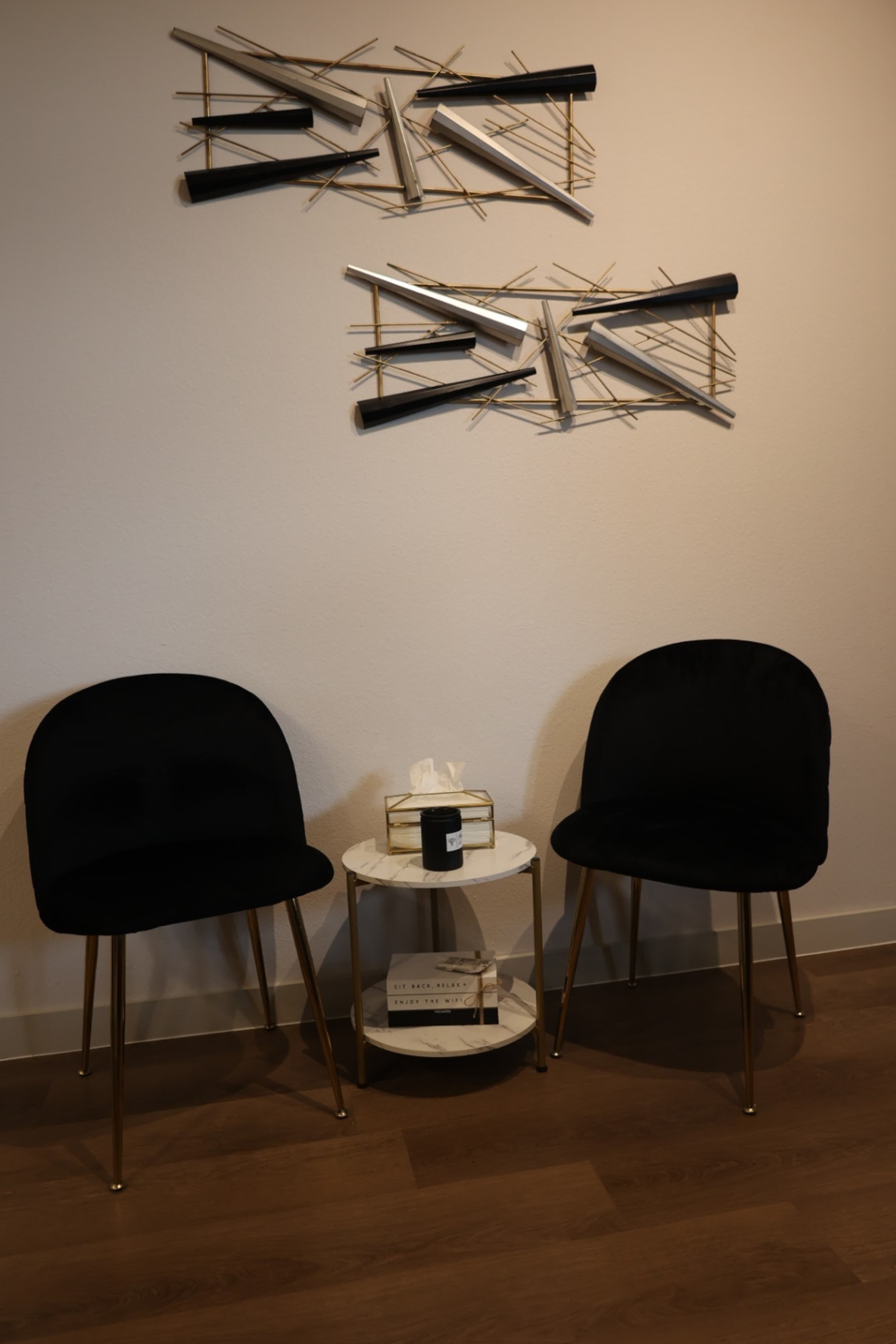 Two black chairs are positioned beside a small round table with decorative items, against a wall featuring abstract art.