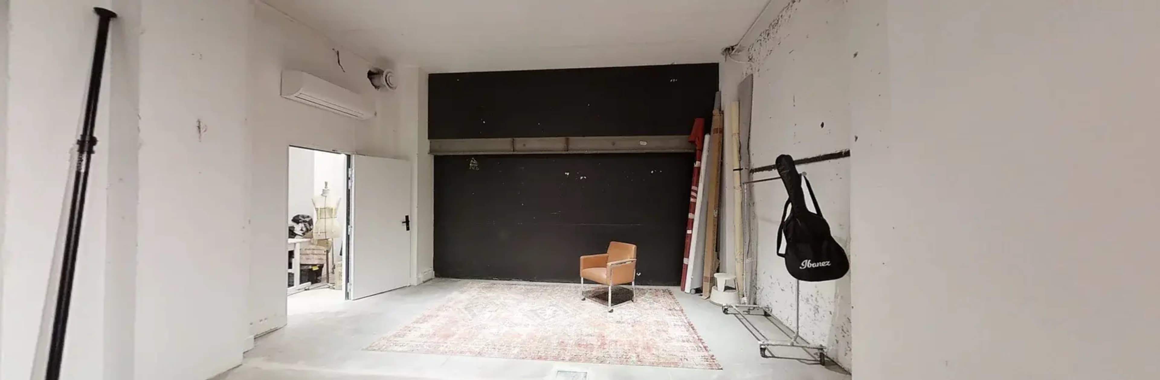 An empty room features a single chair on a rug, a black wall, and a ladder against the wall.