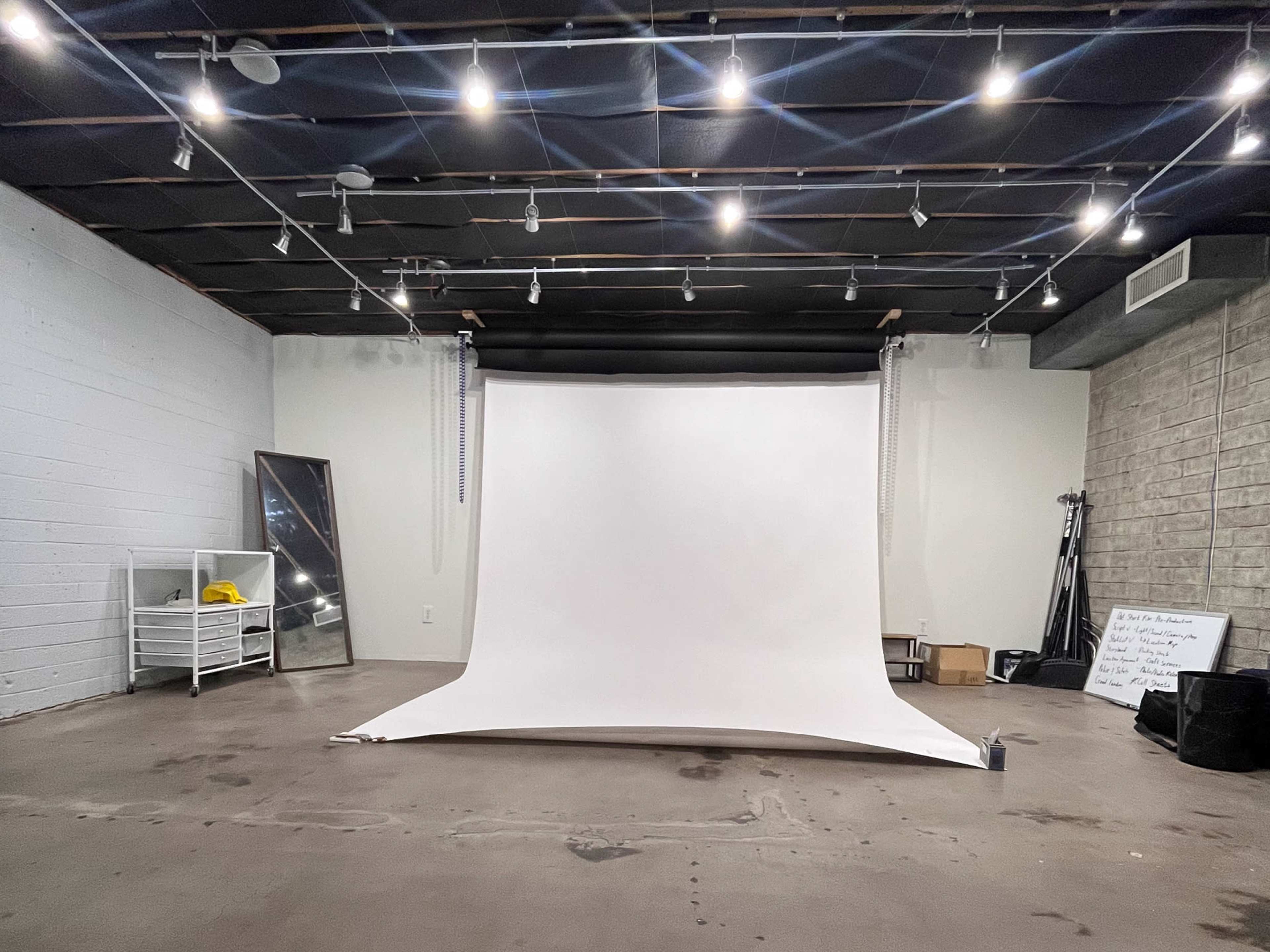 A photography studio with a large white backdrop, overhead lights, and minimalist fixtures along the walls.